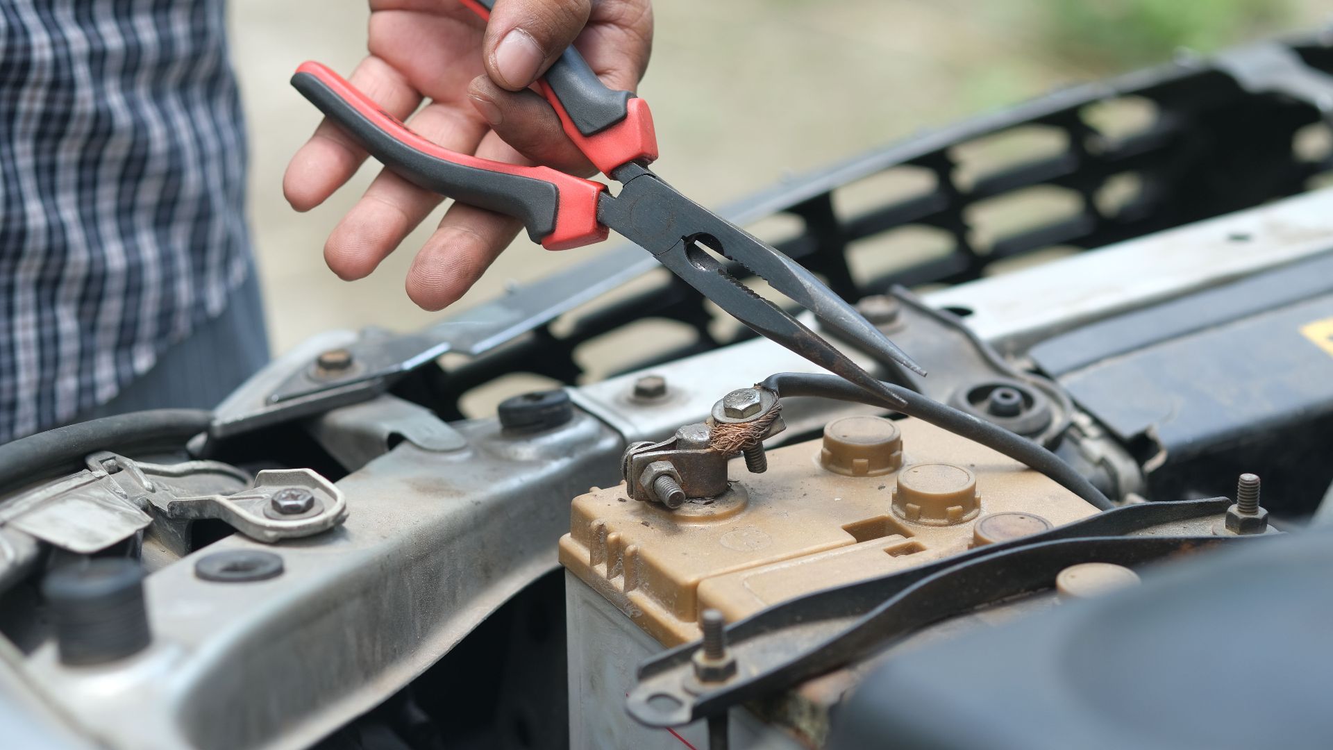 Person using pliers to check a car battery in an outdoor setting.