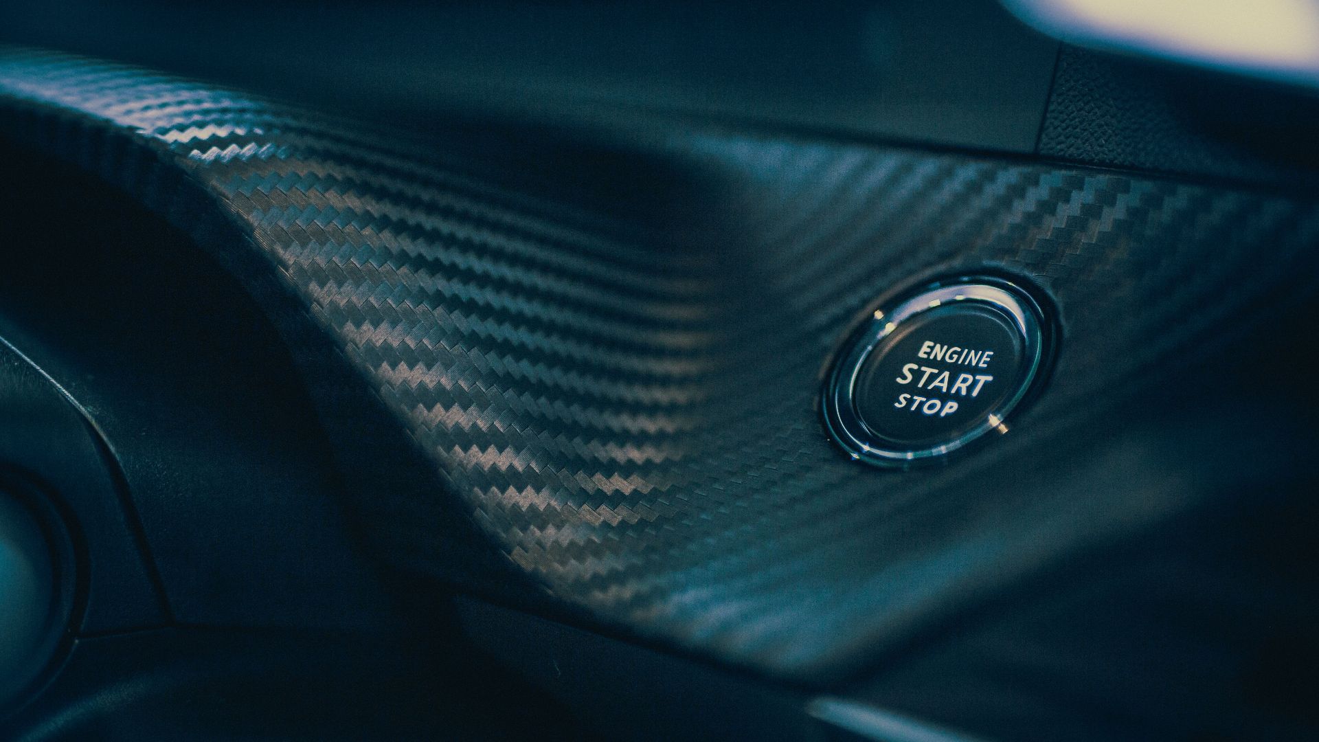Detailed view of a car's engine start button set in sleek carbon fiber interior.