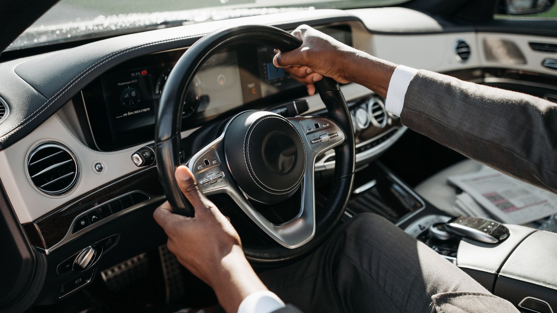 Close-up of hands on steering wheel in a luxury car with dashboard and controls.
