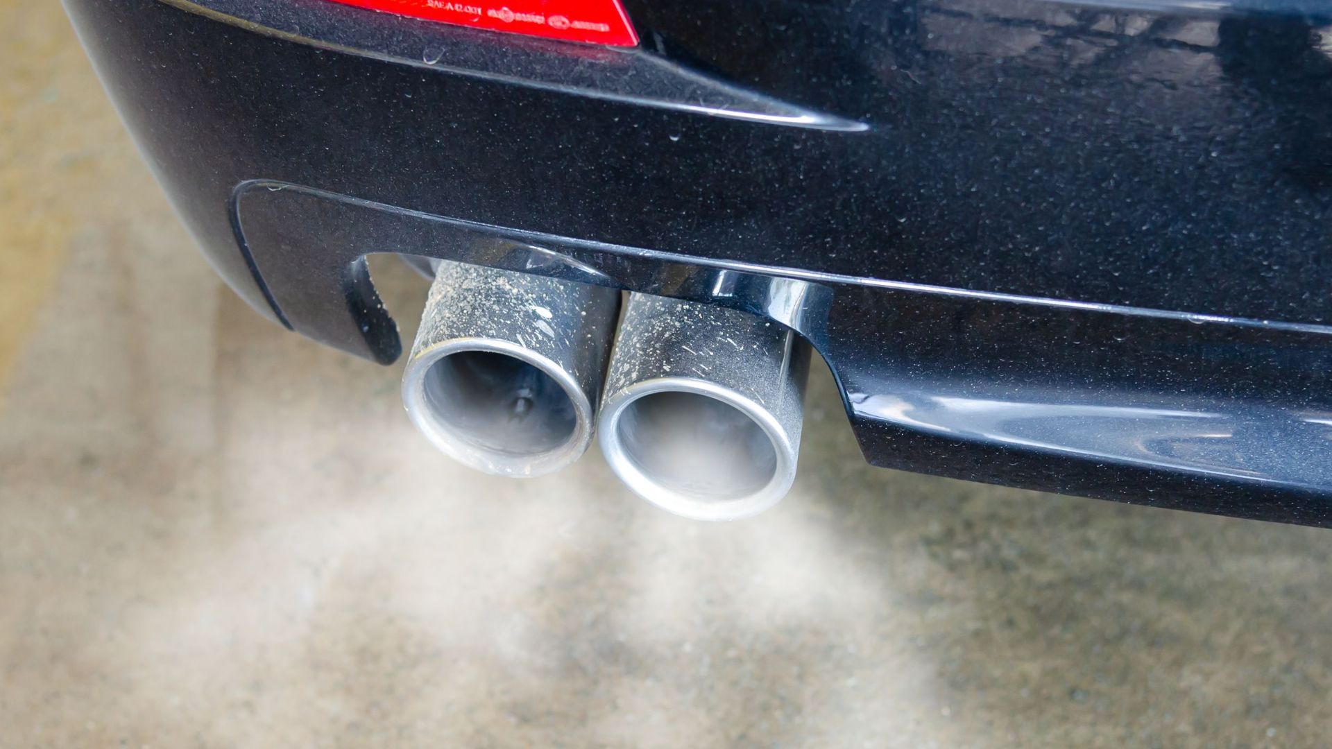 Close-up of a car's exhaust pipes emitting visible smoke, highlighting air pollution.