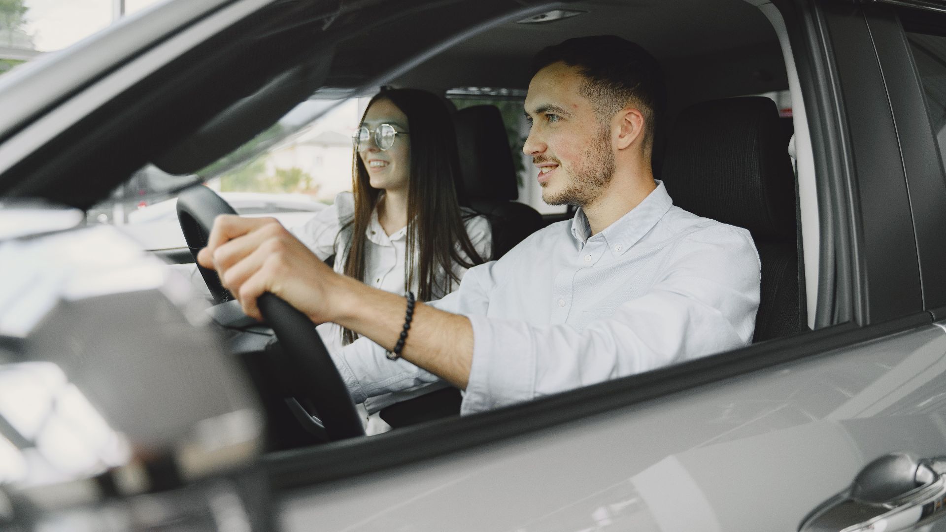 A young couple smiling while driving together in a modern car interior.