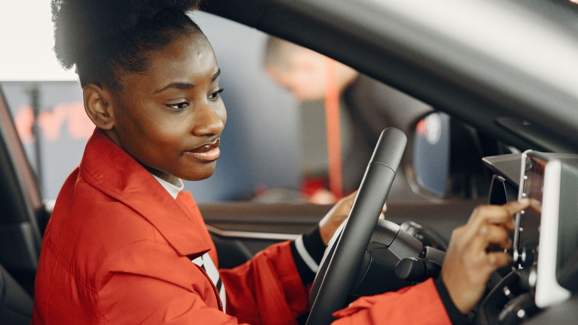 Young woman in red coat using touch screen in car interior.