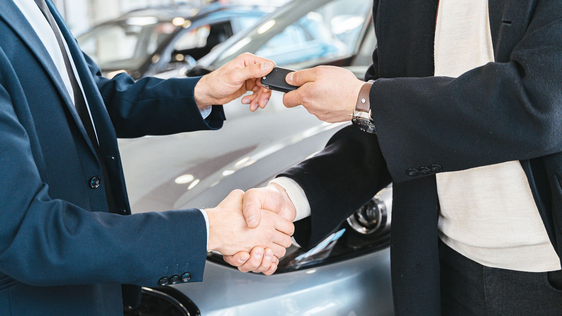 Two businessmen shaking hands and exchanging car keys in a dealership. Symbolizes a successful deal.