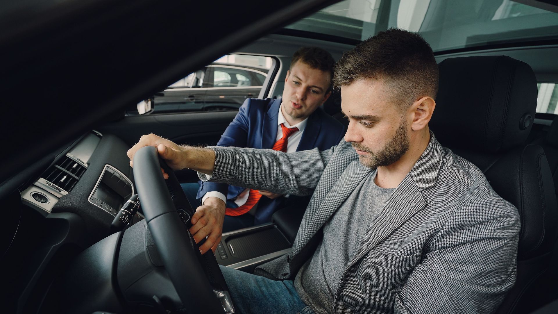 Salesman demonstrating car features to potential buyer inside vehicle showroom.