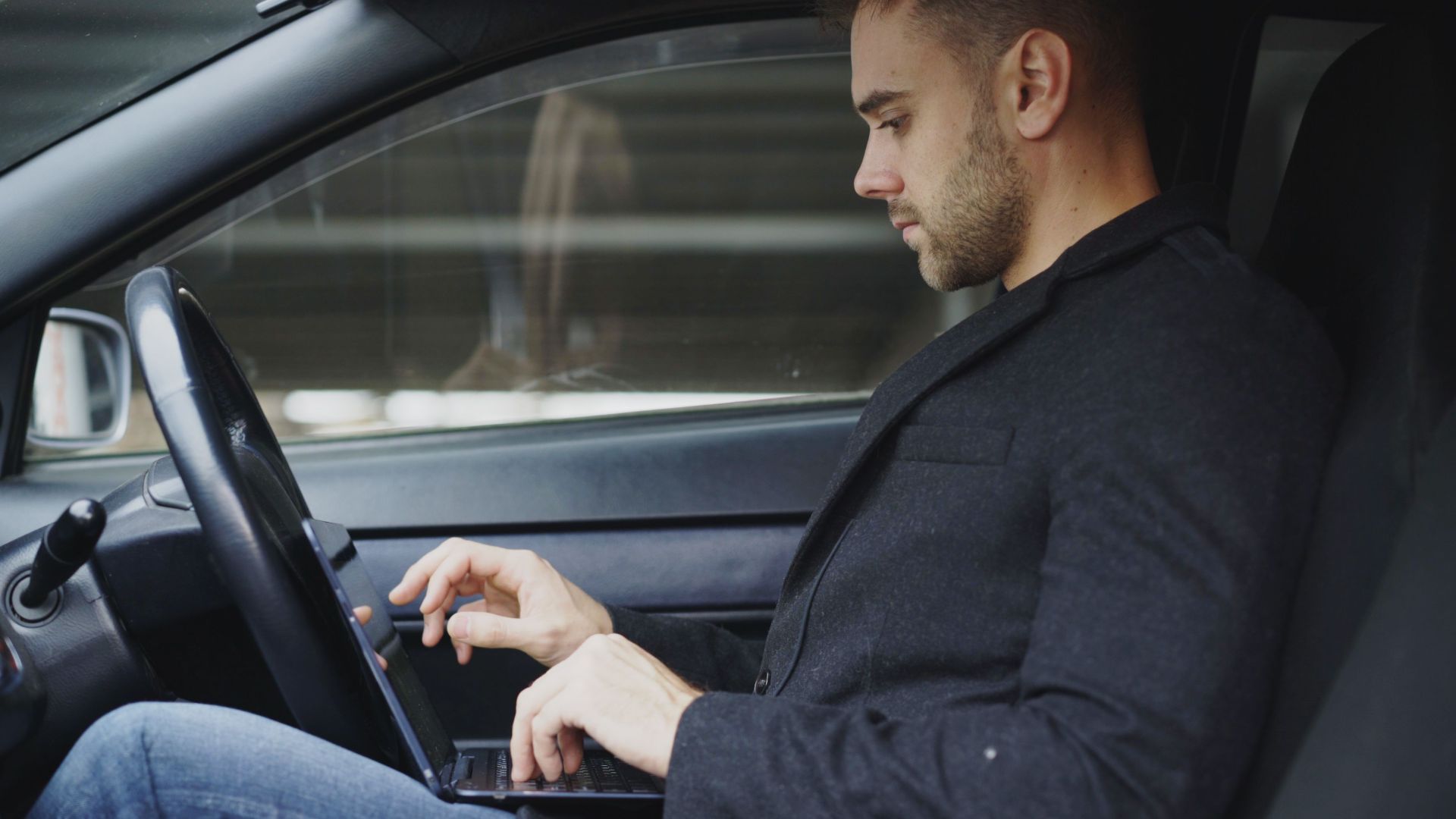 Focused businessman using laptop in car, multitasking and working on the go.
