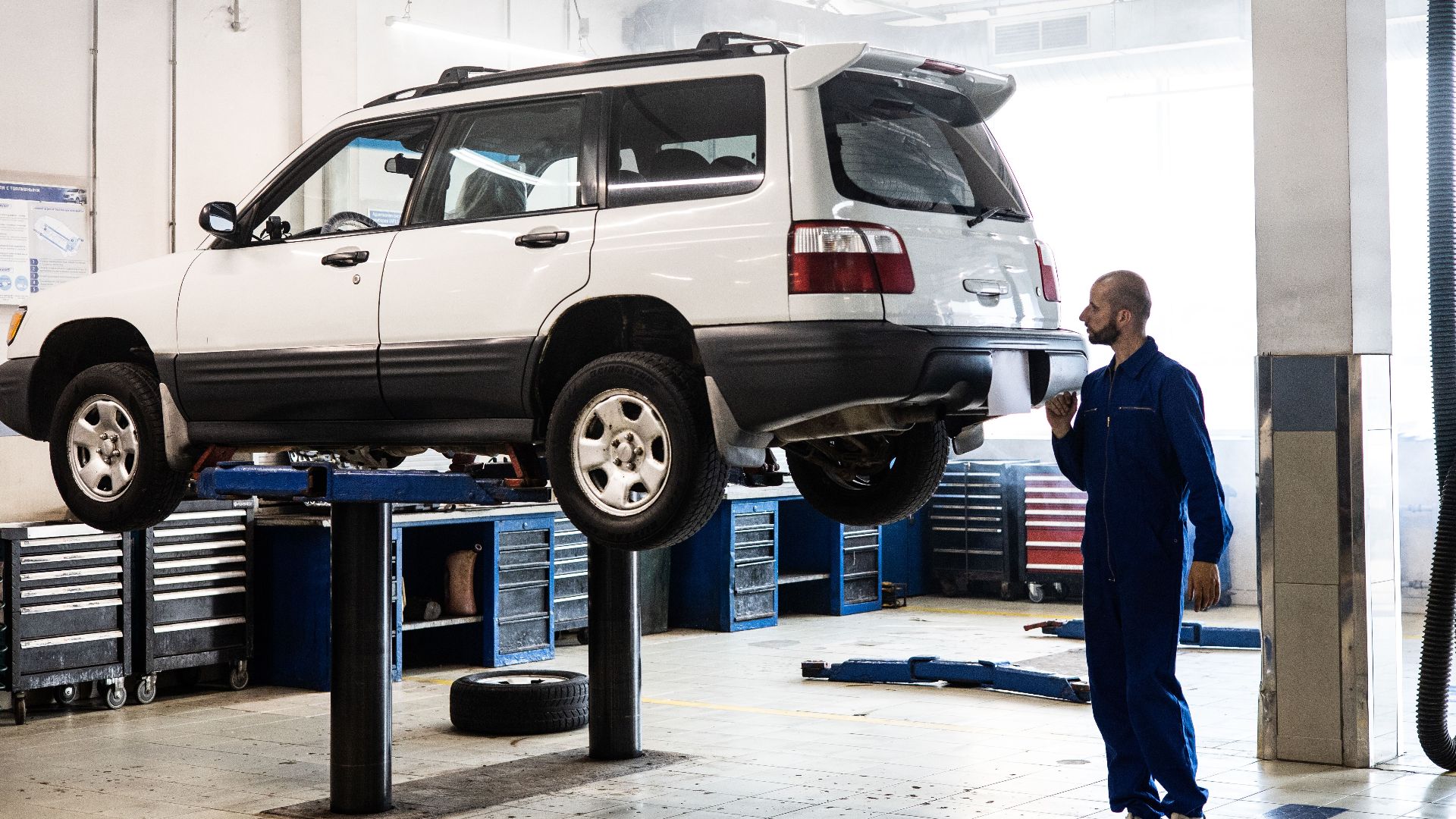 Mechanic inspecting a lifted SUV in a modern auto repair garage.
