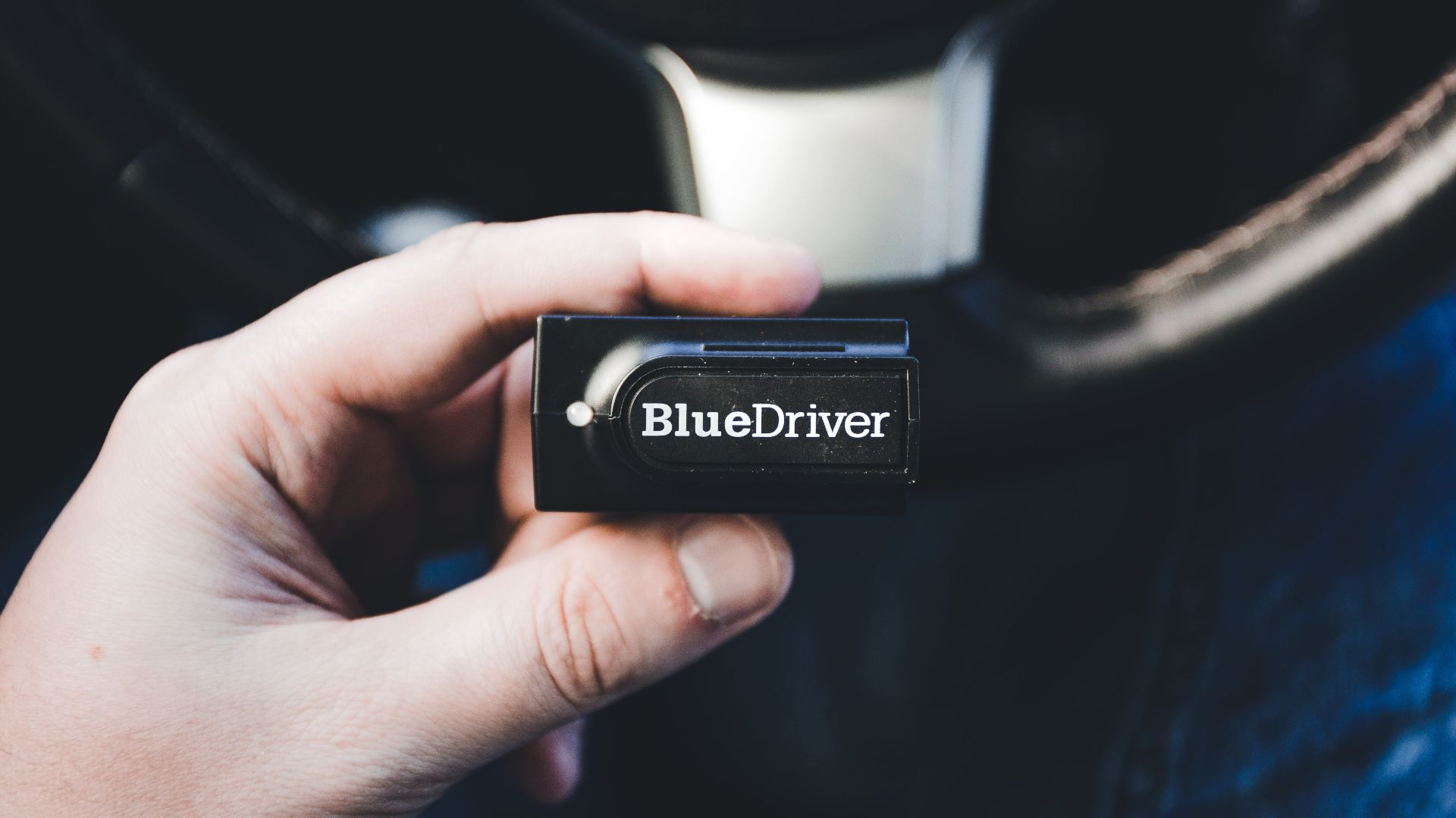 Close-up of a hand holding a BlueDriver wireless diagnostic tool inside a vehicle.