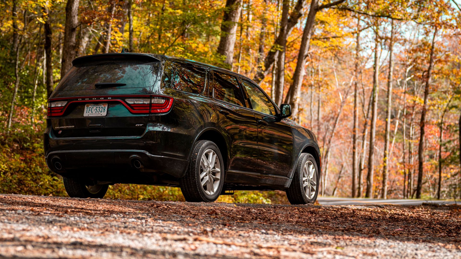 A sleek black SUV parked on a gravel road surrounded by autumn foliage, exuding a sense of adventure.