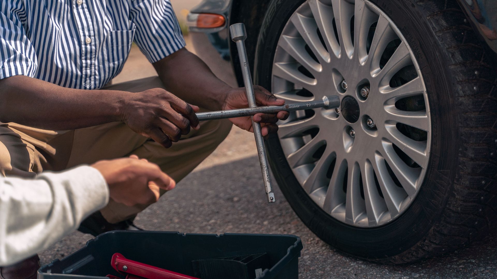 An adult demonstrating how to change a tire to a teenager, focusing on teamwork and learning.