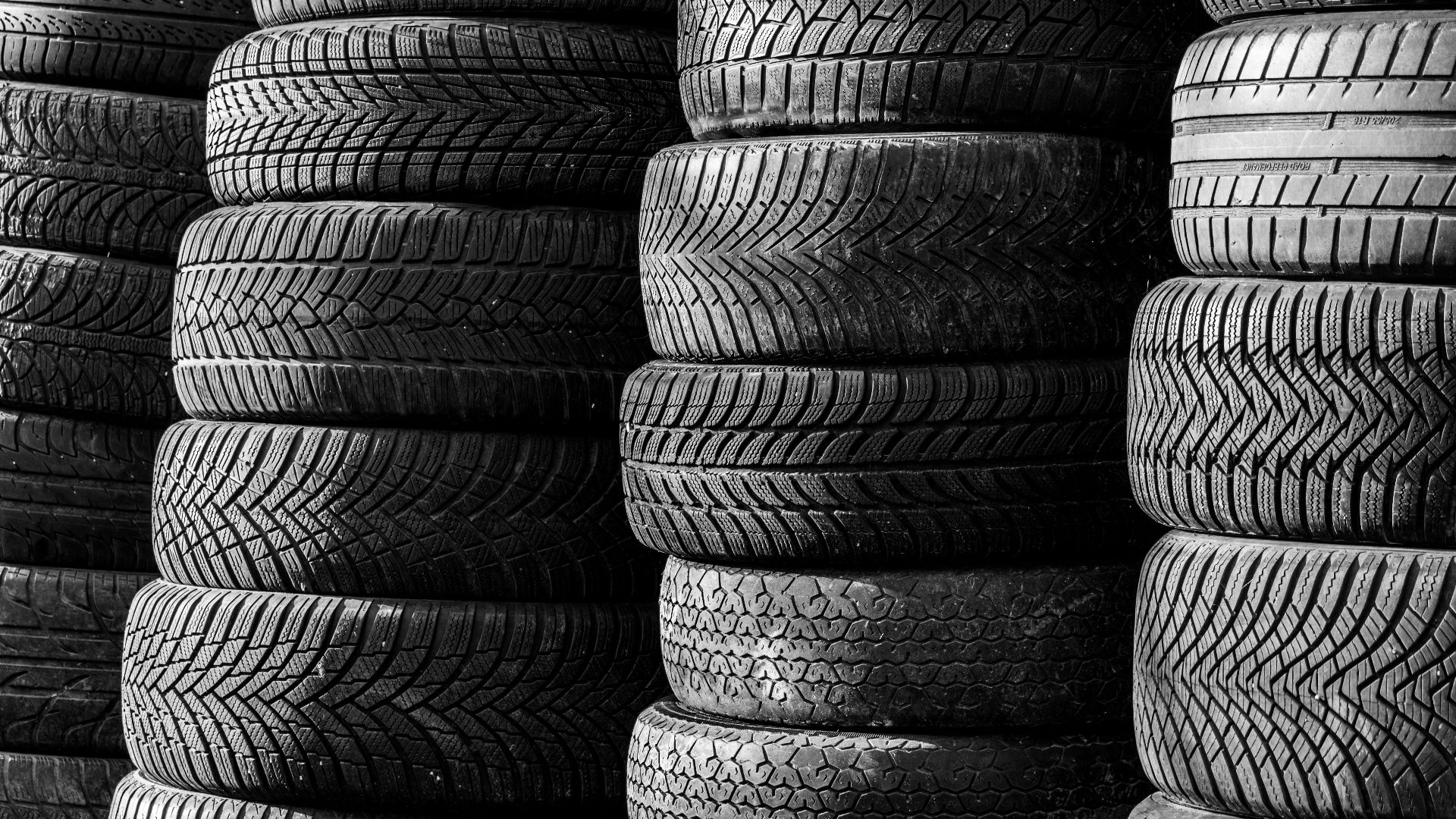 Black and white image of stacked vehicle tires showcasing various tread patterns.