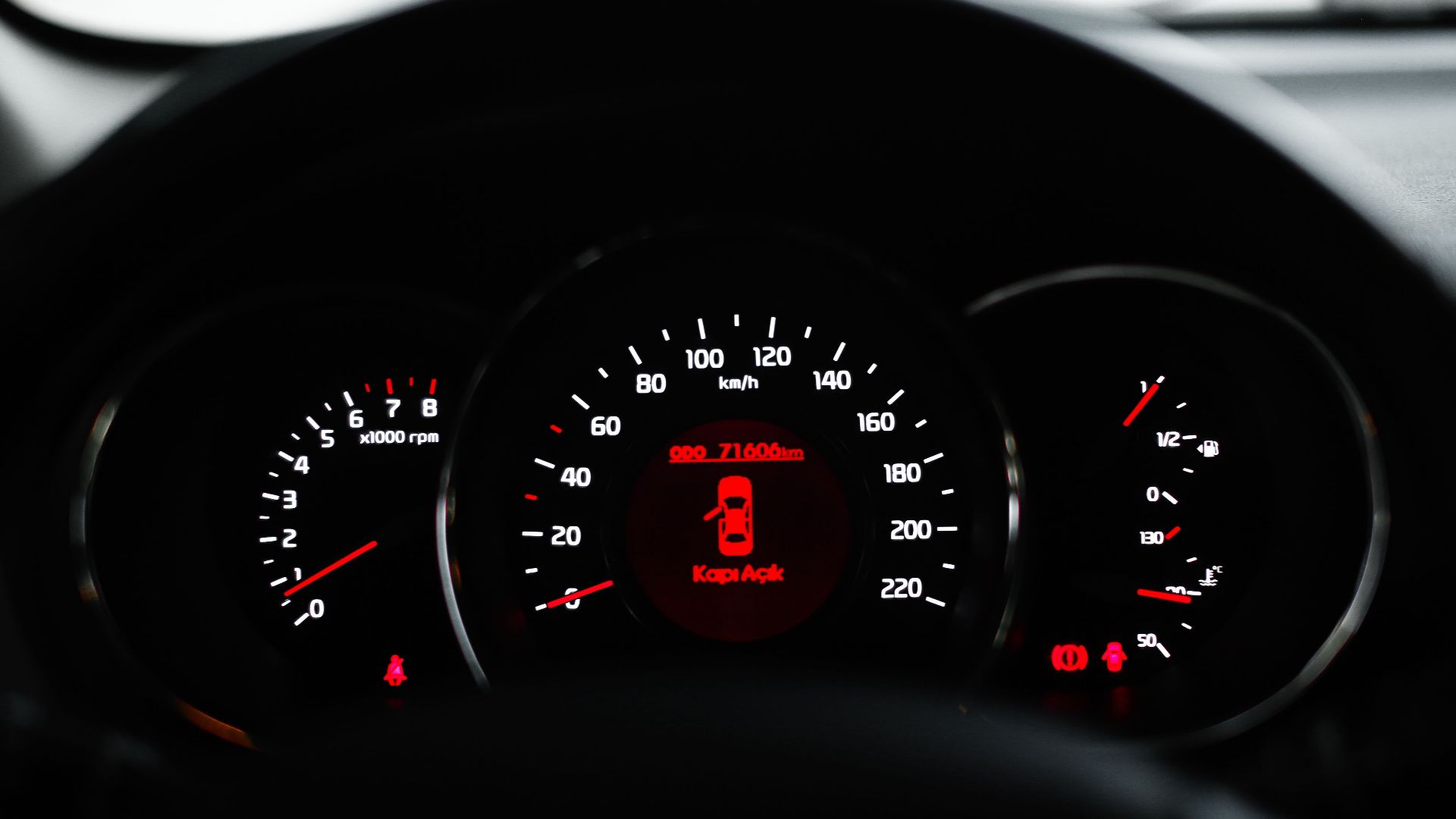 Car dashboard showing a warning light with various dials and gauges in focus.