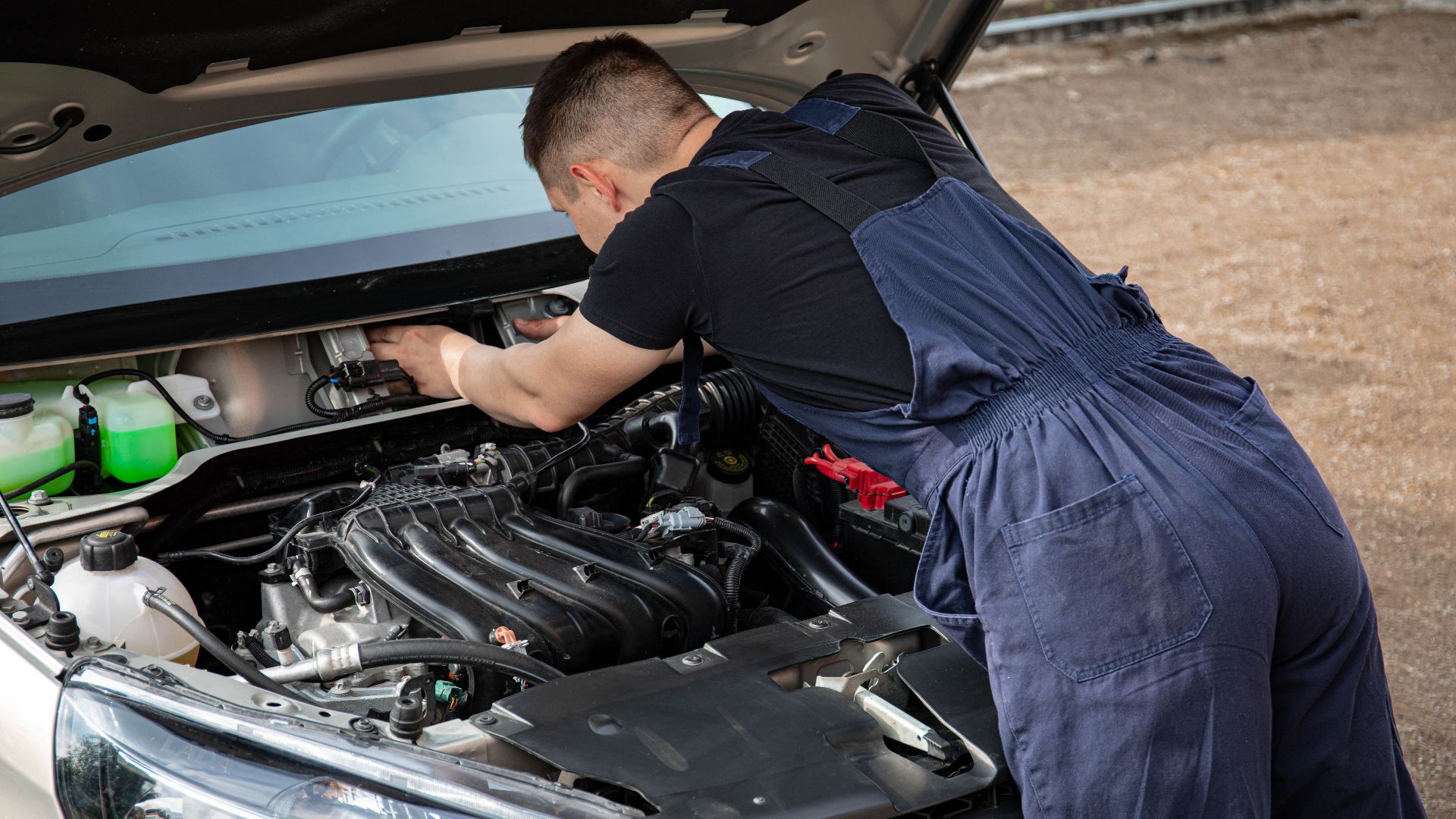 Mechanic in overalls fixing a car engine outdoors, showcasing automotive repair skills.