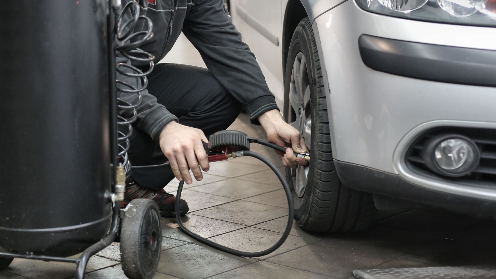 Mechanic inspecting and adjusting tire pressure in an auto repair shop.