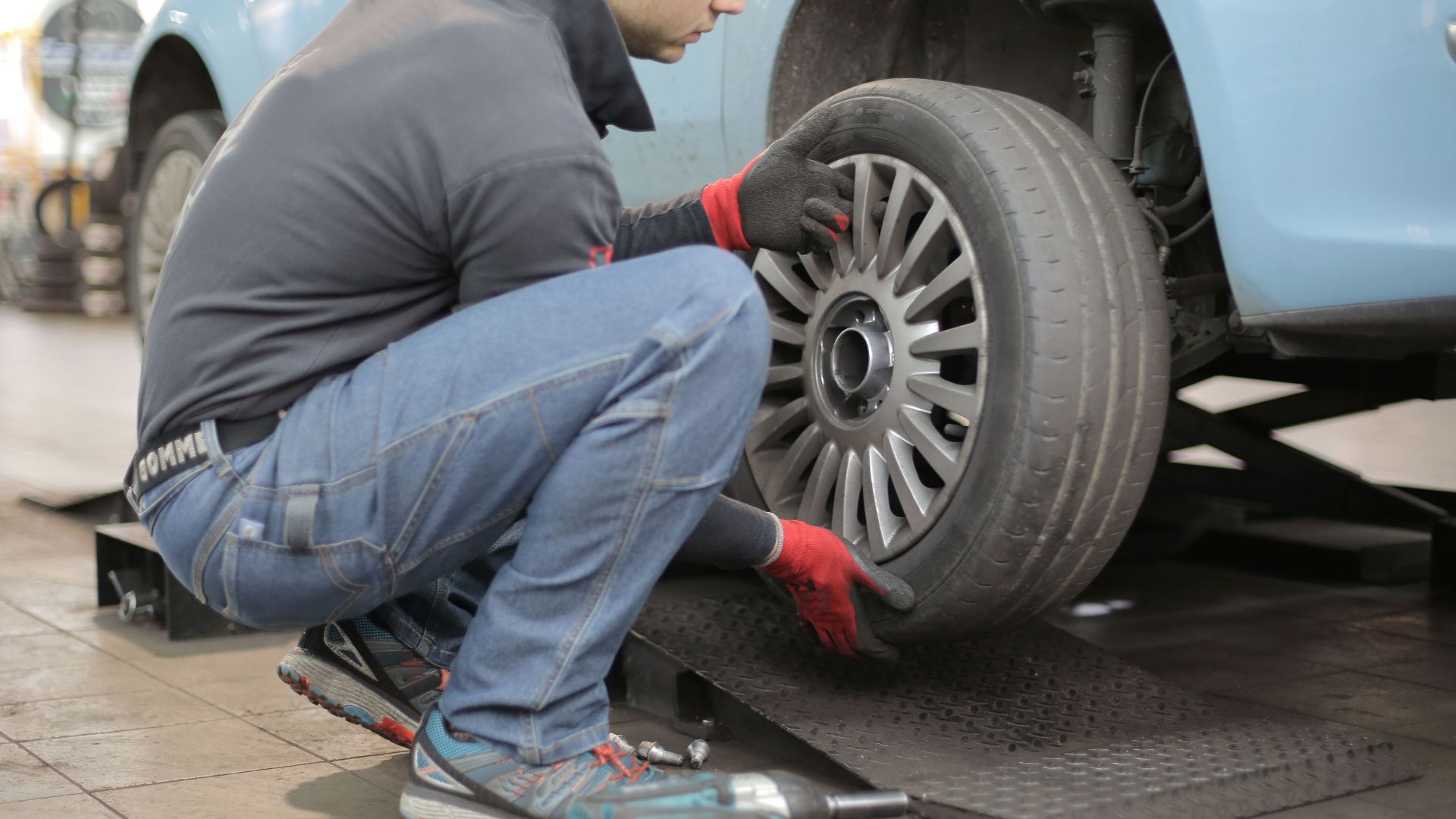 Mechanic changing a car tire indoors, using tools for vehicle maintenance.