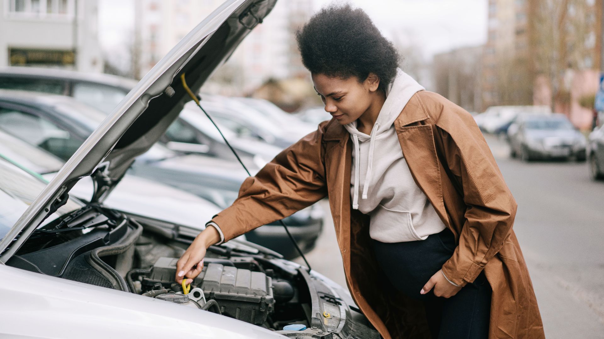 A pregnant woman inspects a car engine outdoors, showcasing independence and car maintenance skills.