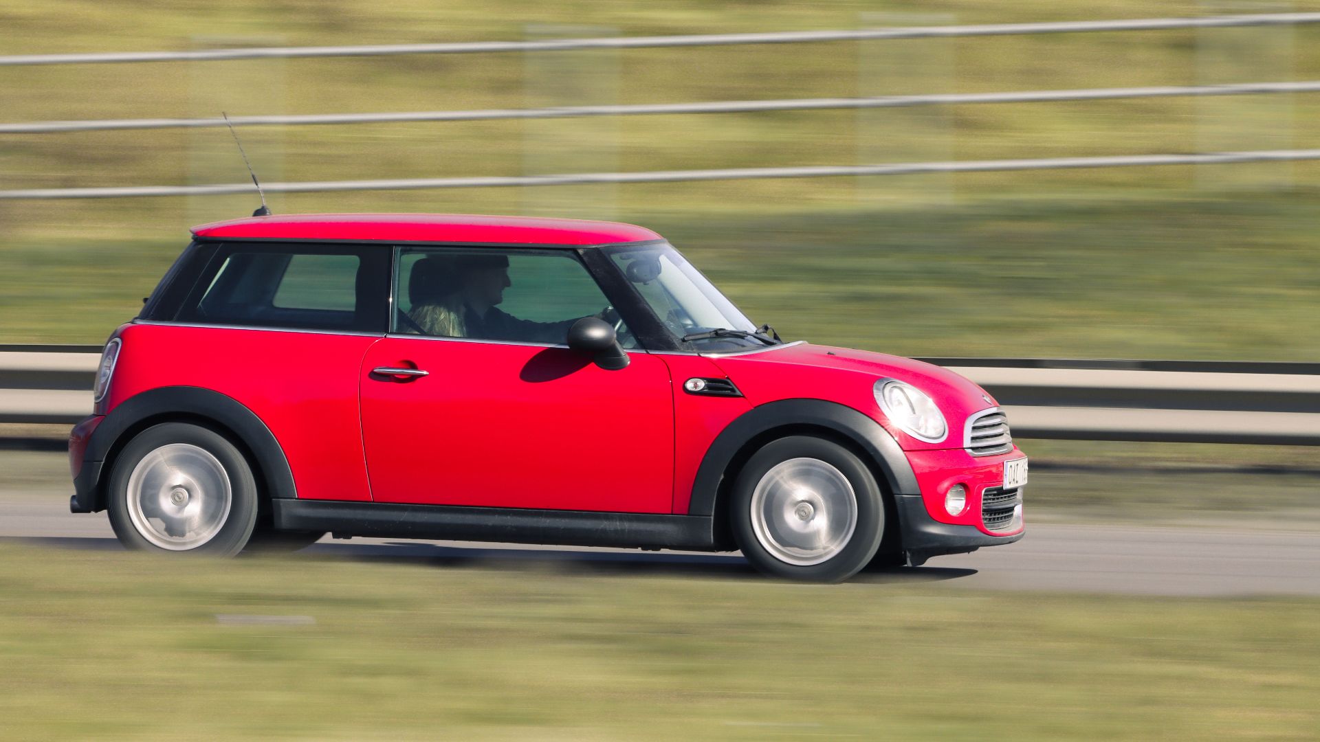A red Mini Cooper car in motion captured on a road in Jönköping, Sweden.