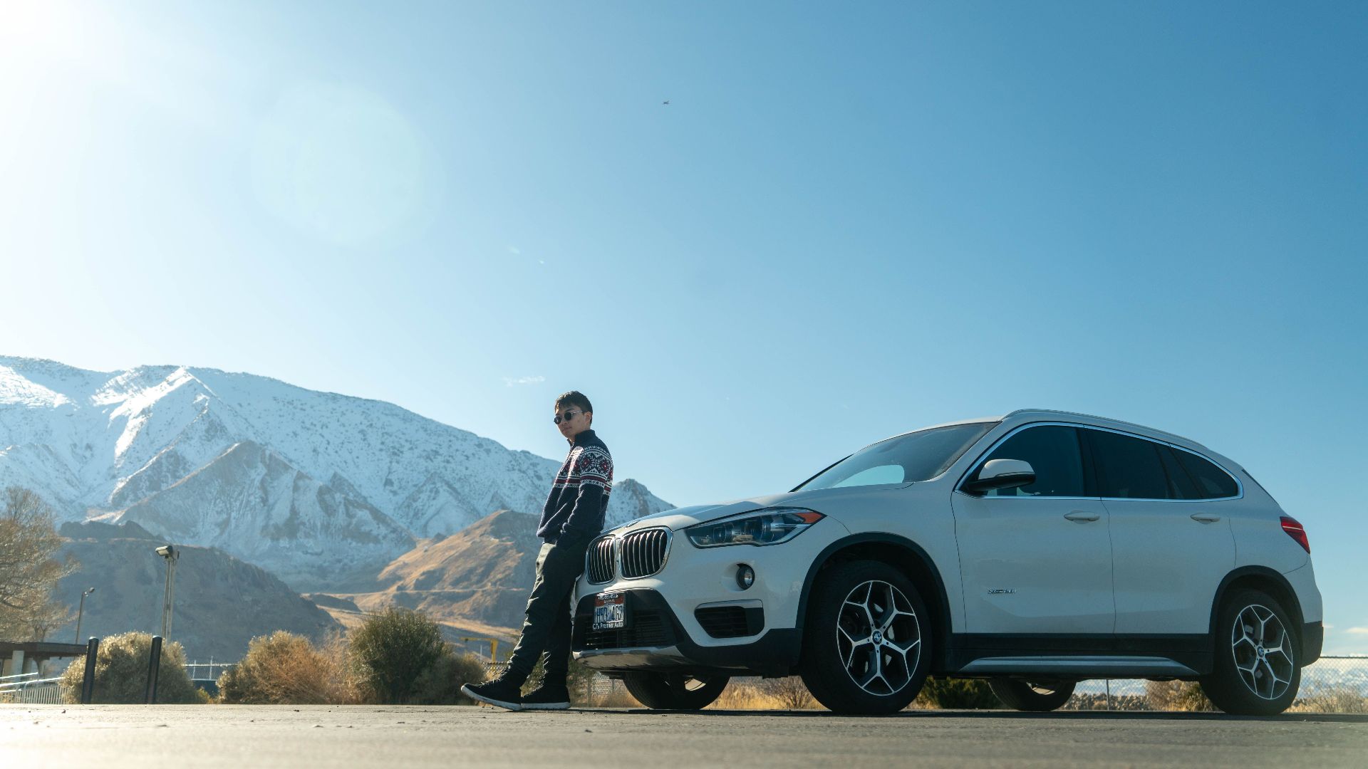 A person stands beside a white SUV with snow-covered mountains in Utah as a backdrop.