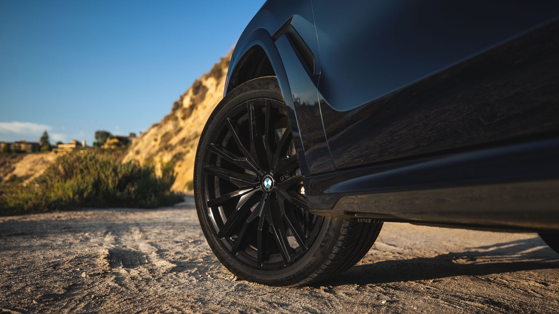 Close-up of a luxury black car with alloy wheels parked outdoors at sunset.