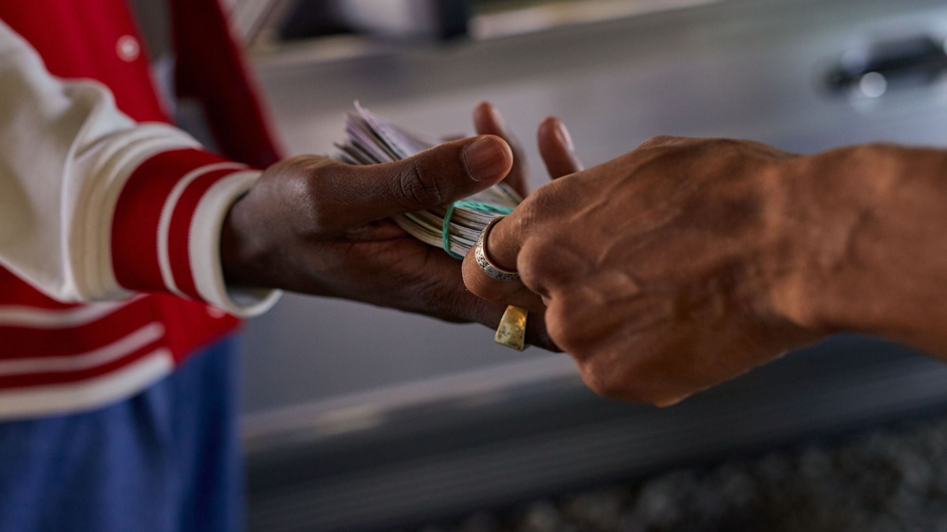 A detailed shot of two hands exchanging a bundle of cash outside by a car.