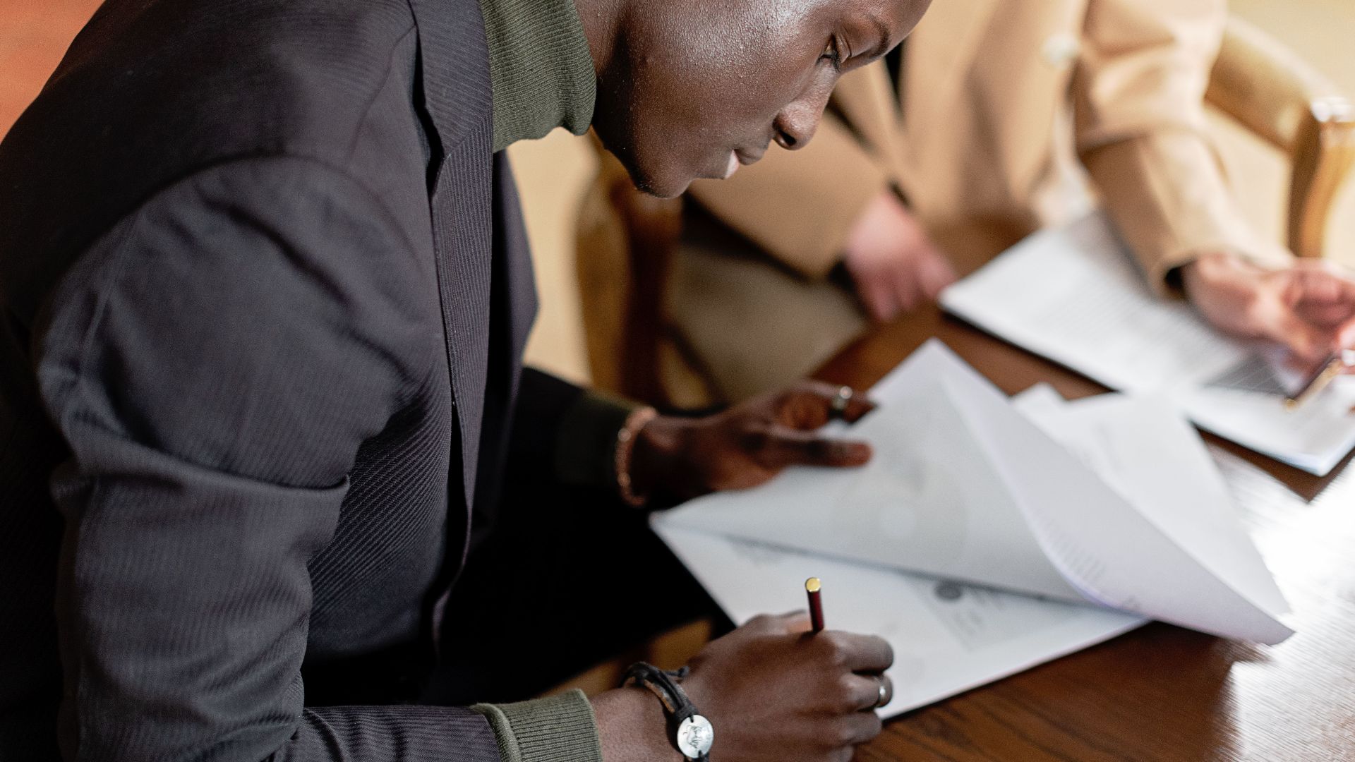 African American man focused on signing important business documents at a desk.