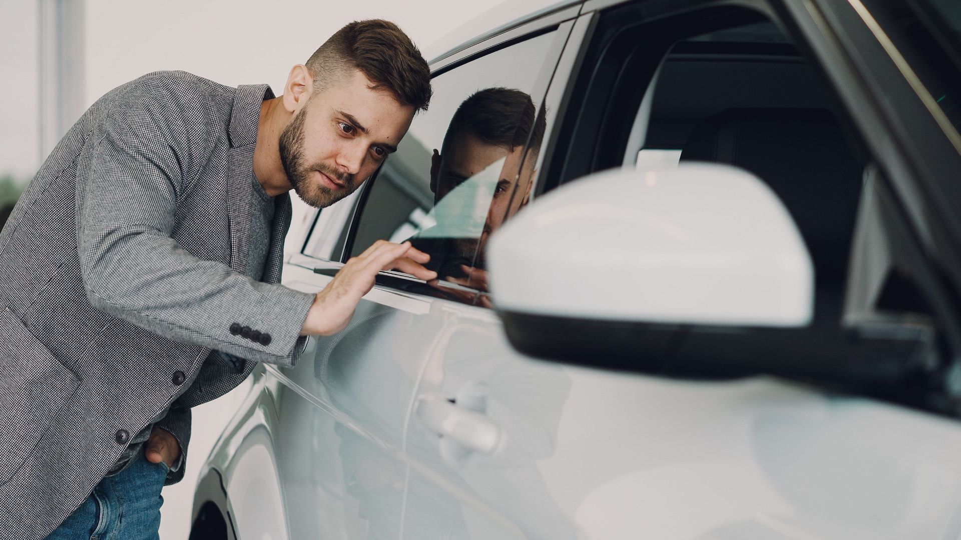 Man carefully examining a modern white car at a dealership showroom.