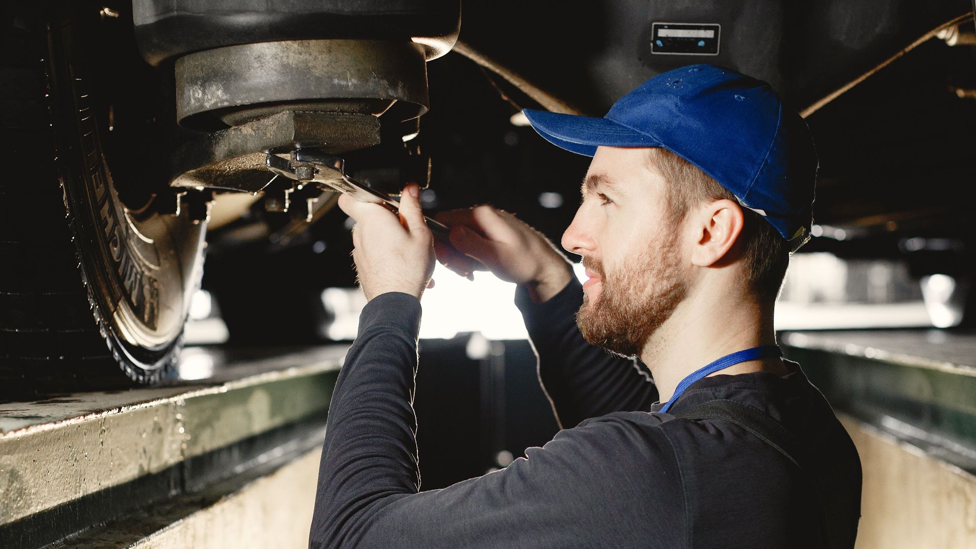 An auto mechanic working on a vehicle's underbody in a workshop setting.