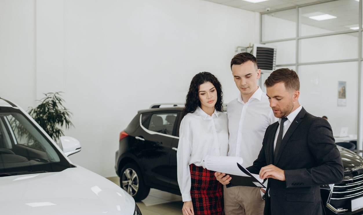 Car dealer showing car to couple in showroom.