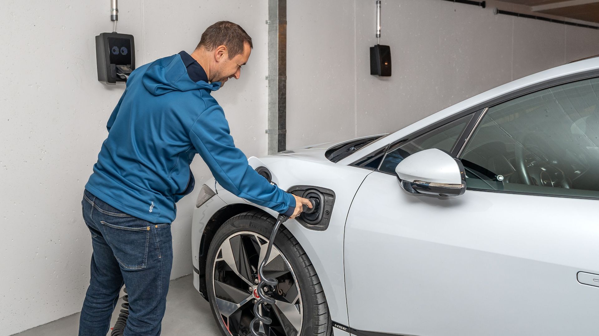 A man connects an electric car to a charging station in a modern indoor garage setting.