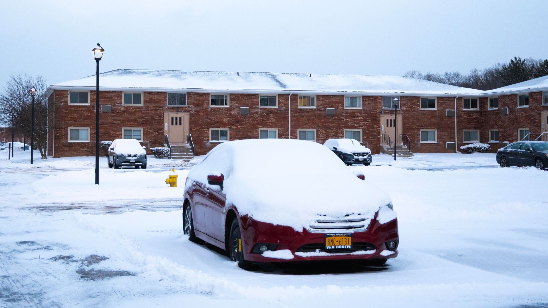 A snowy urban scene with parked cars and brick apartments on a winter day.