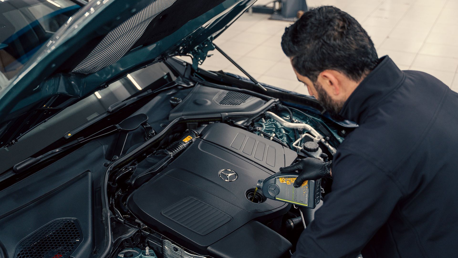 Mechanic inspecting and filling engine oil in a car at an indoor service center.