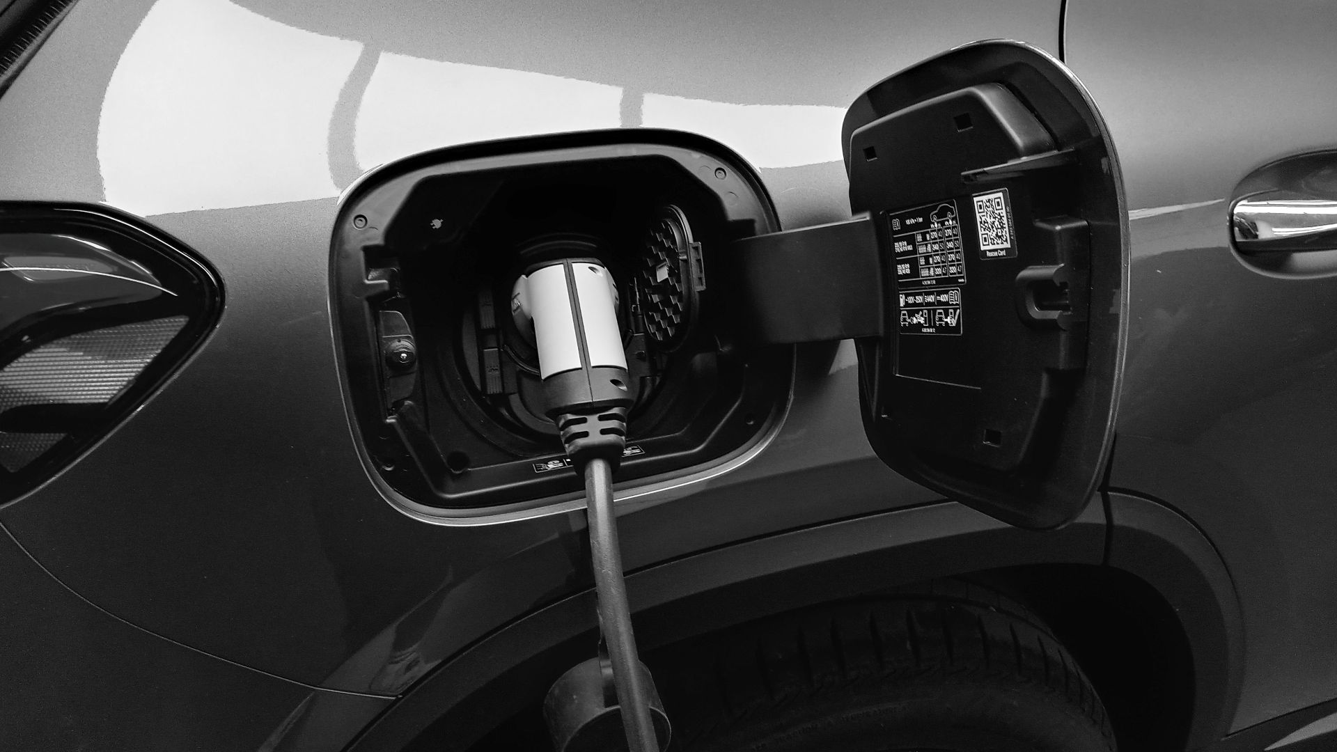 Close-up black and white image of an electric vehicle charging at a station.