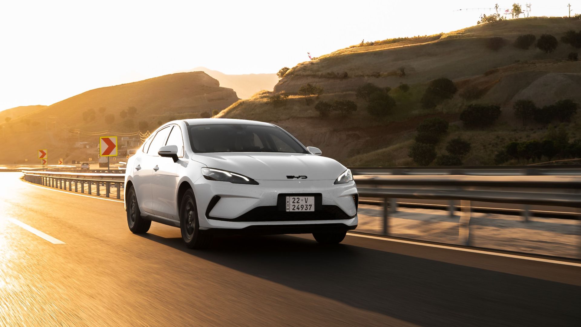 White electric car cruising on a sunlit highway, showcasing modern automotive design.