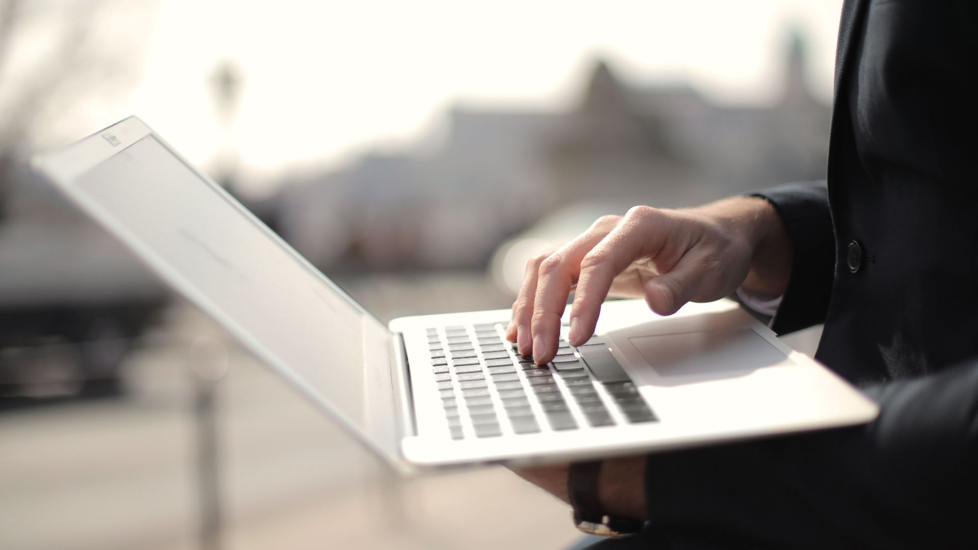 A business professional typing on a laptop in an outdoor setting, symbolizing remote work.