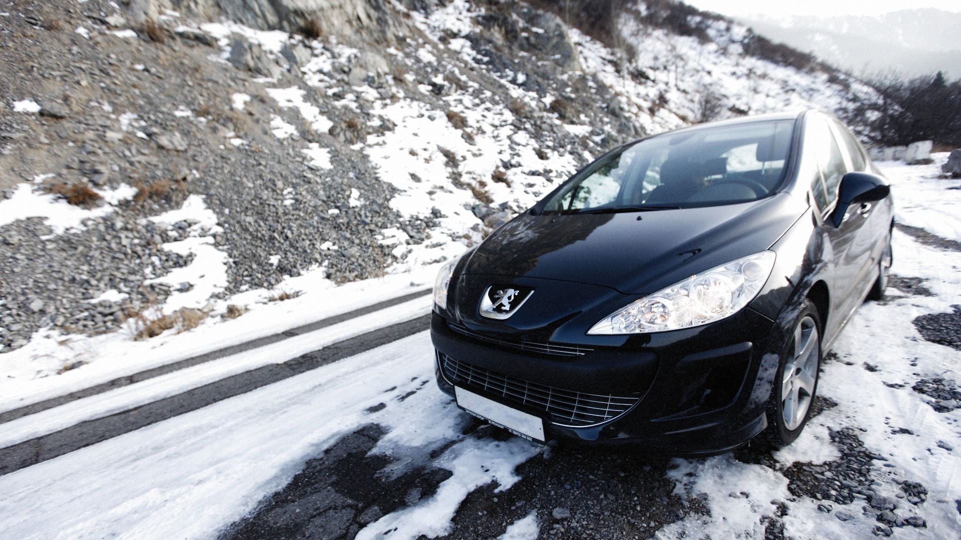 A black car navigates a snowy mountain road, showcasing winter travel and adventure.