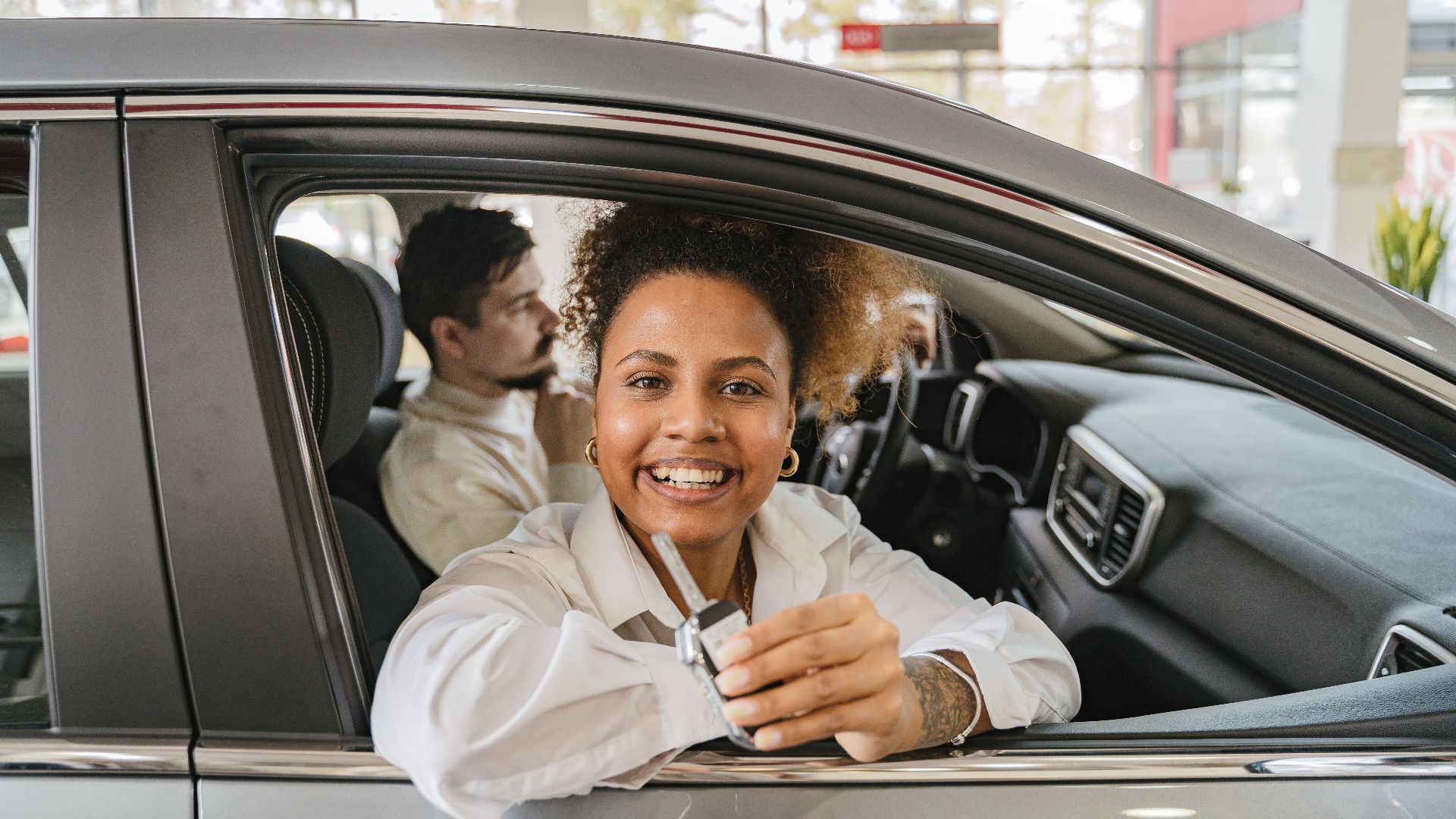 Joyful couple in their new car, holding keys in a dealership showroom, smiling warmly.