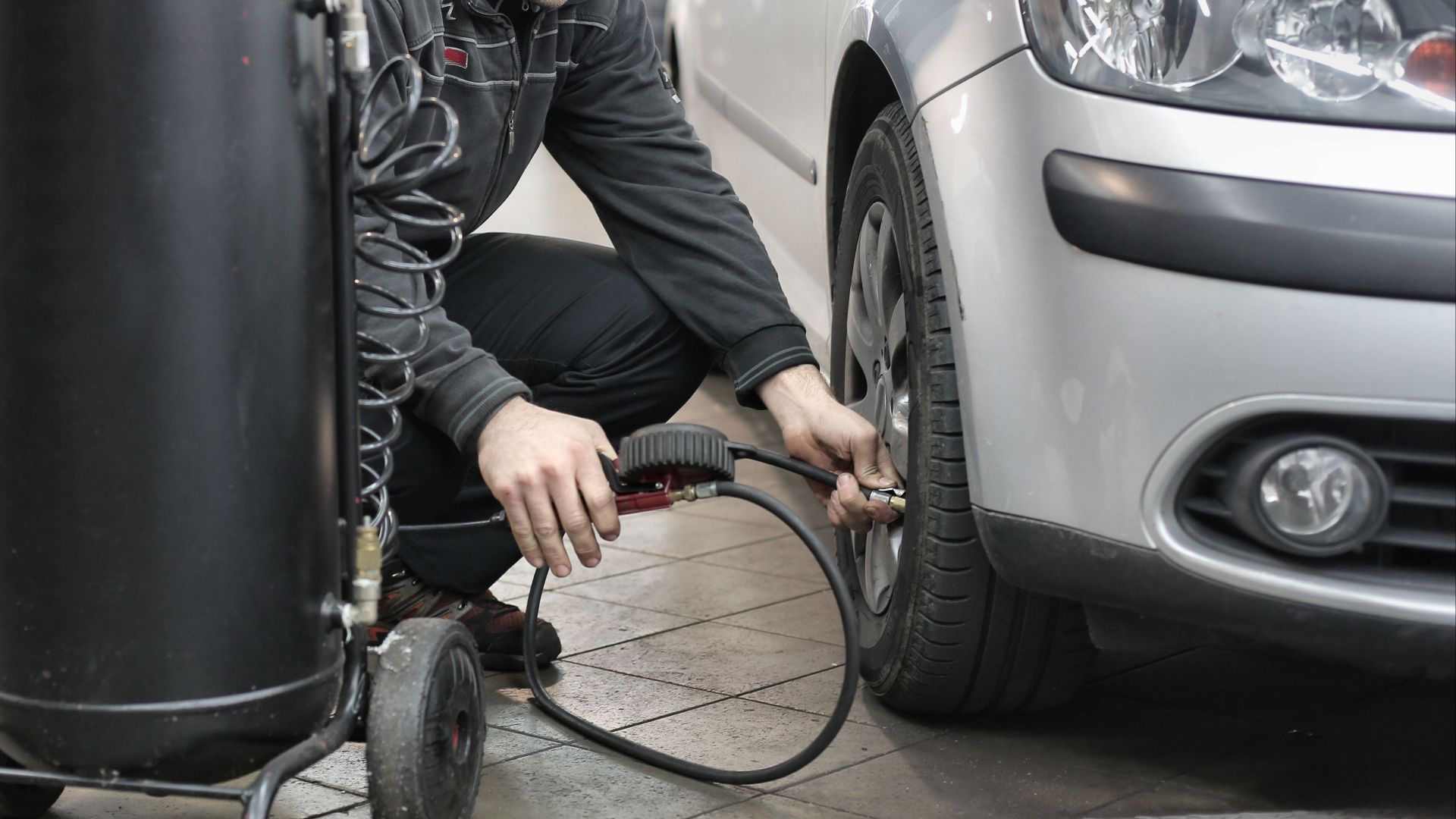 Mechanic inspecting and adjusting tire pressure in an auto repair shop.