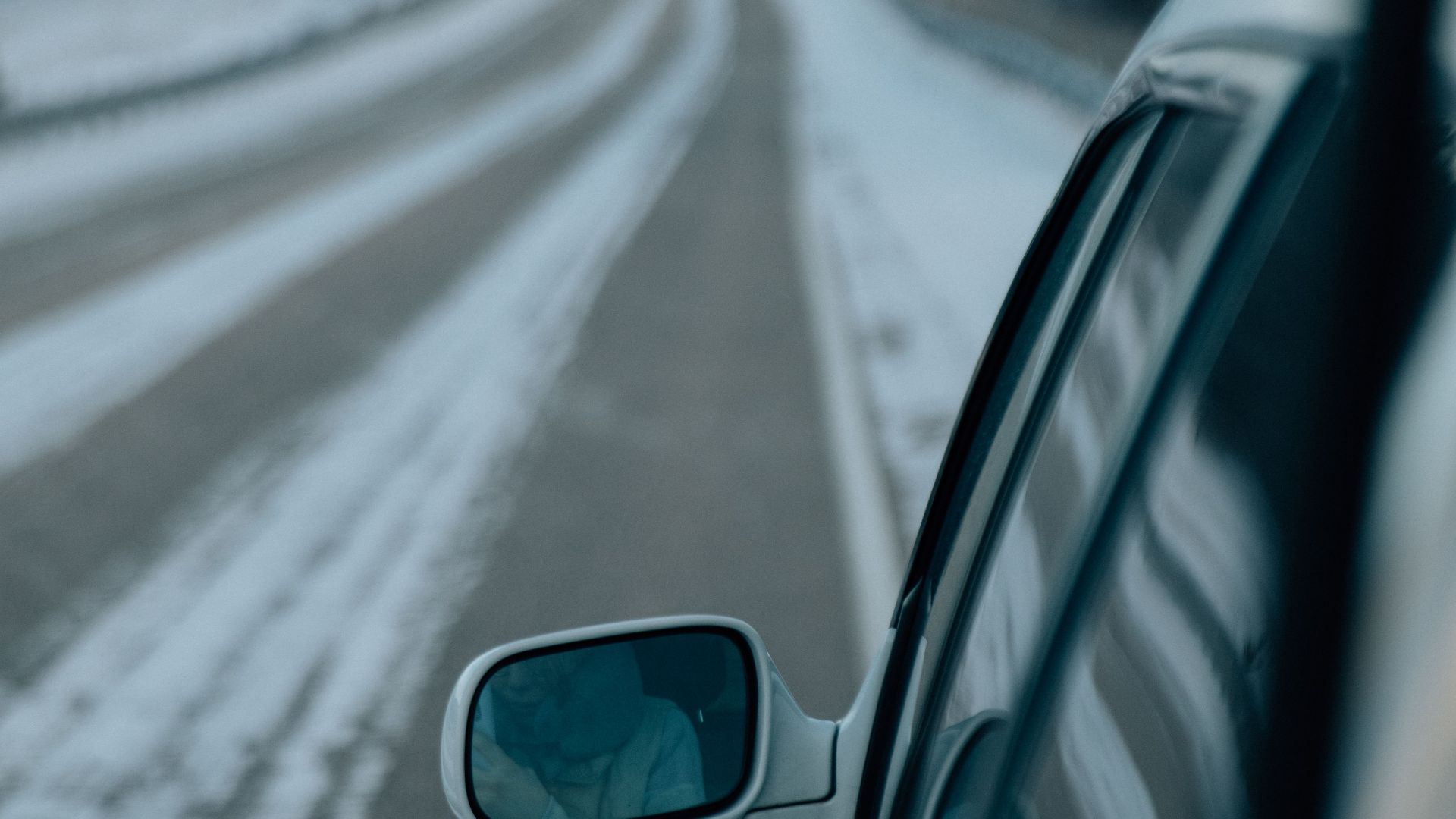 A scenic view from a car on a snowy road, highlighting the rear-view mirror in a winter setting.