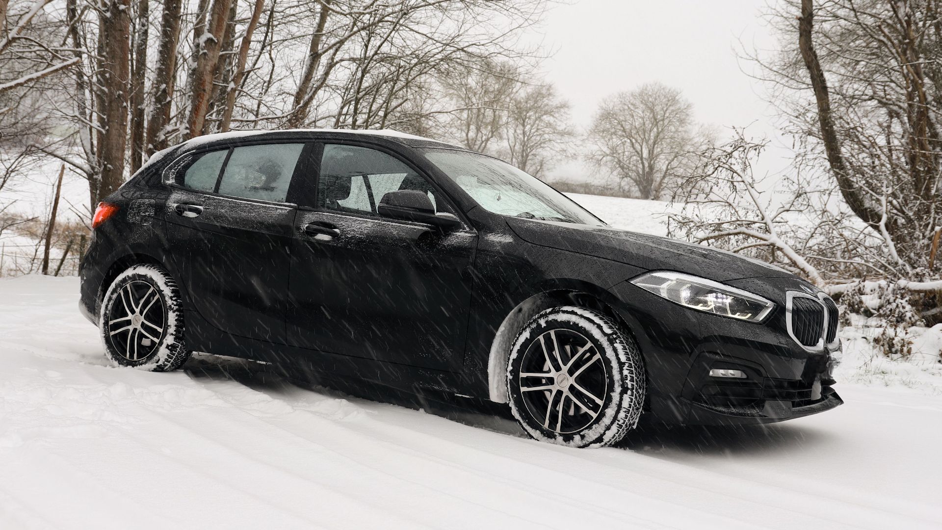 A black car driving through a snowy forest landscape, embodying winter weather's beauty.