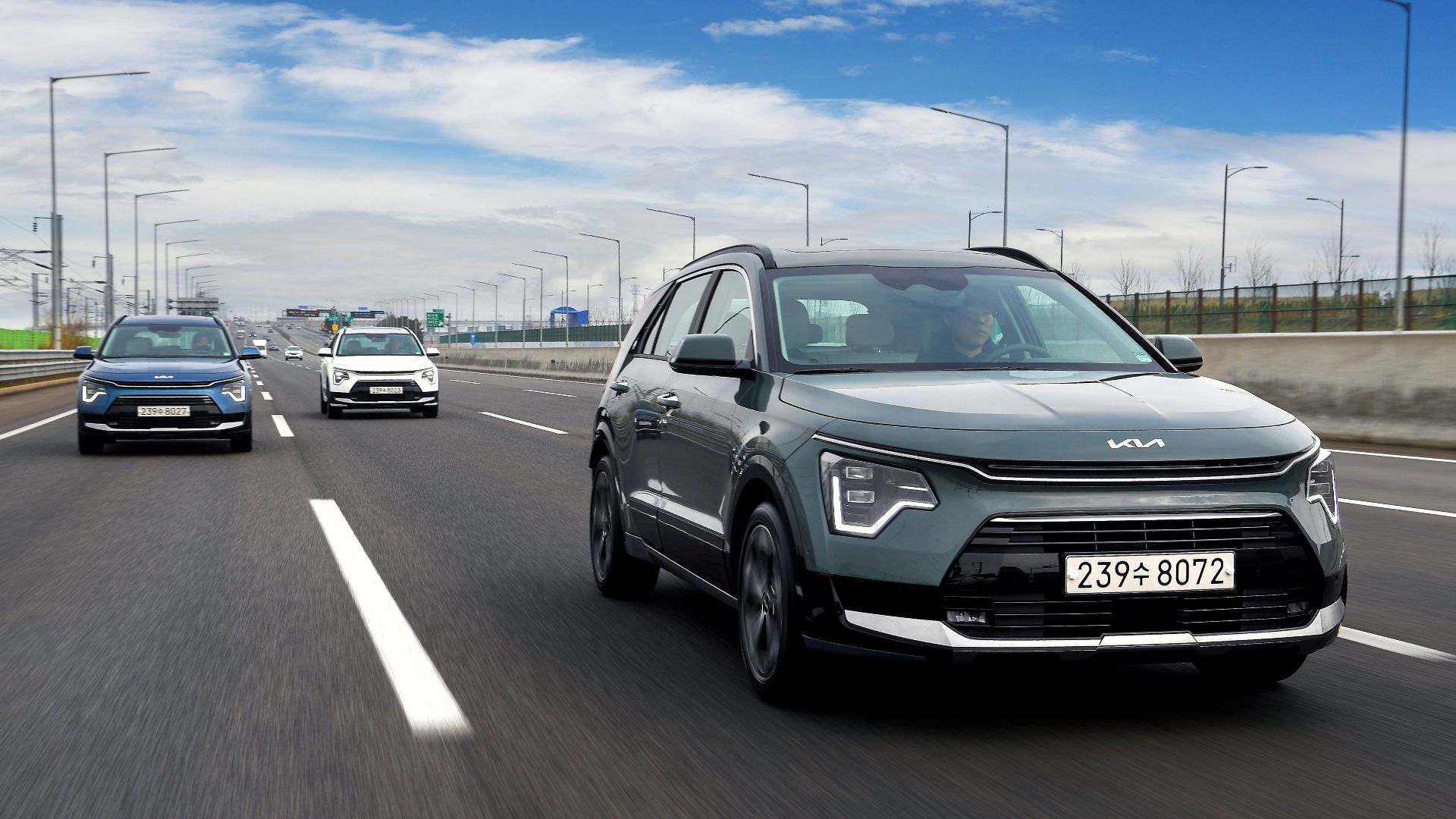Kia Niro SUVs driving on a highway under a bright blue sky, showcasing speed and modern design.