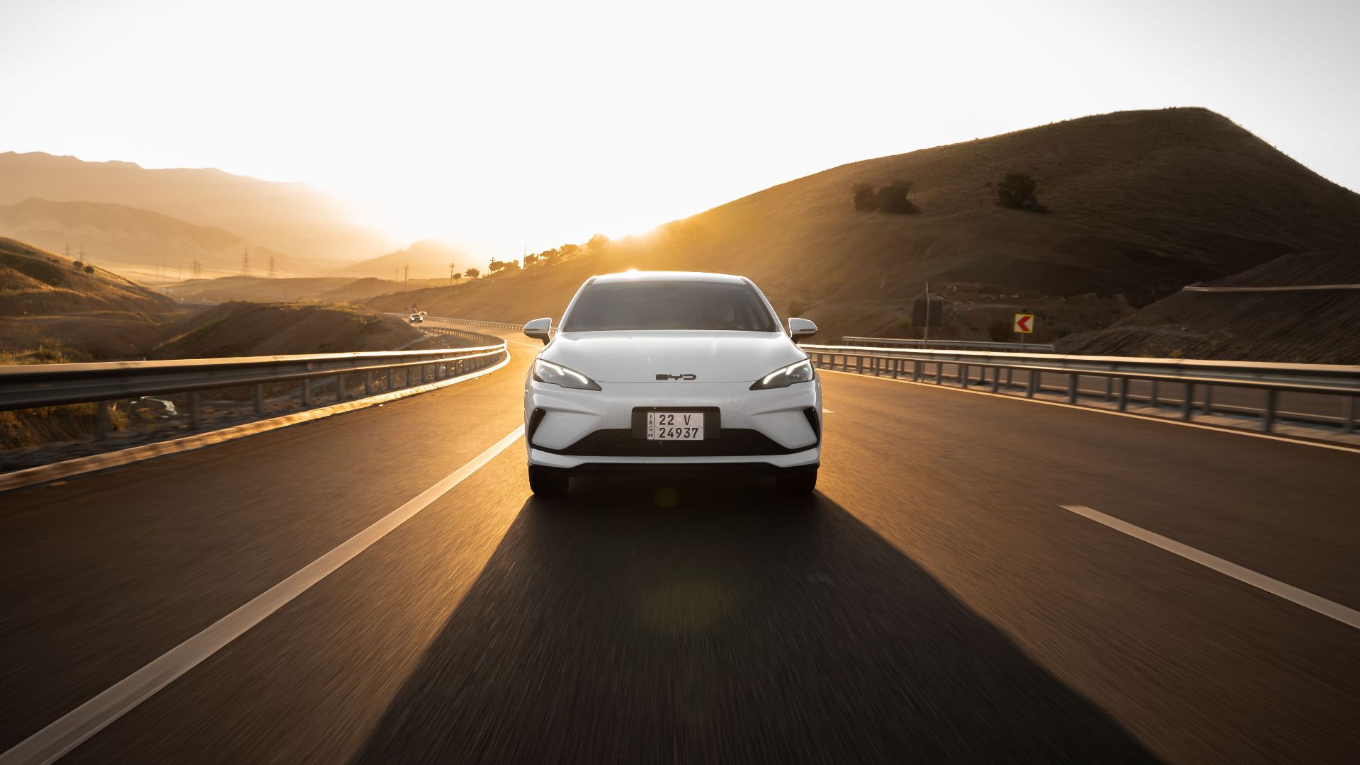 Electric car driving on a scenic highway at sunset, highlighting modern automotive design and sustainable travel.
