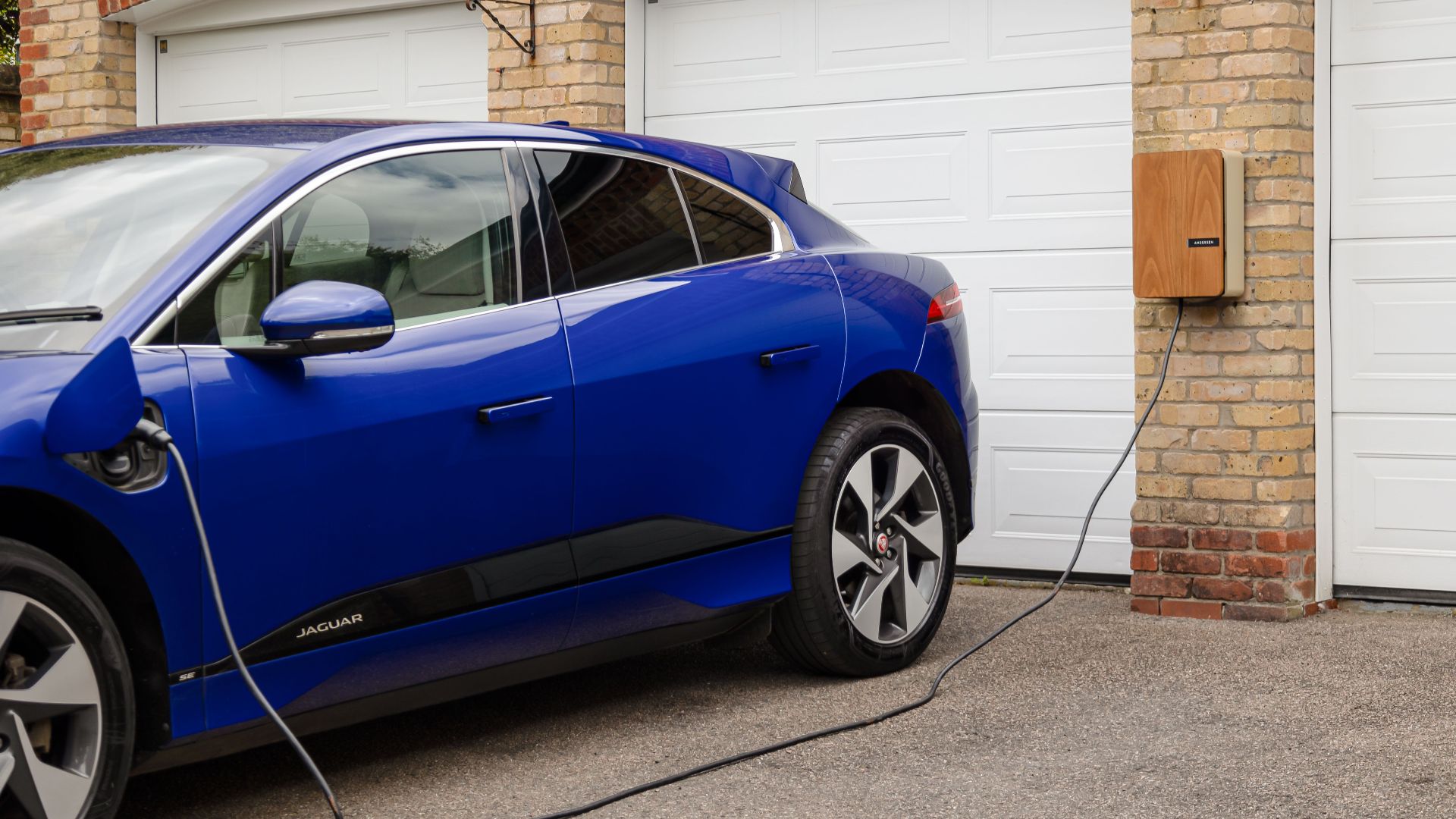 Blue electric vehicle charging at home using wall-mounted unit. Sustainable transportation solution.