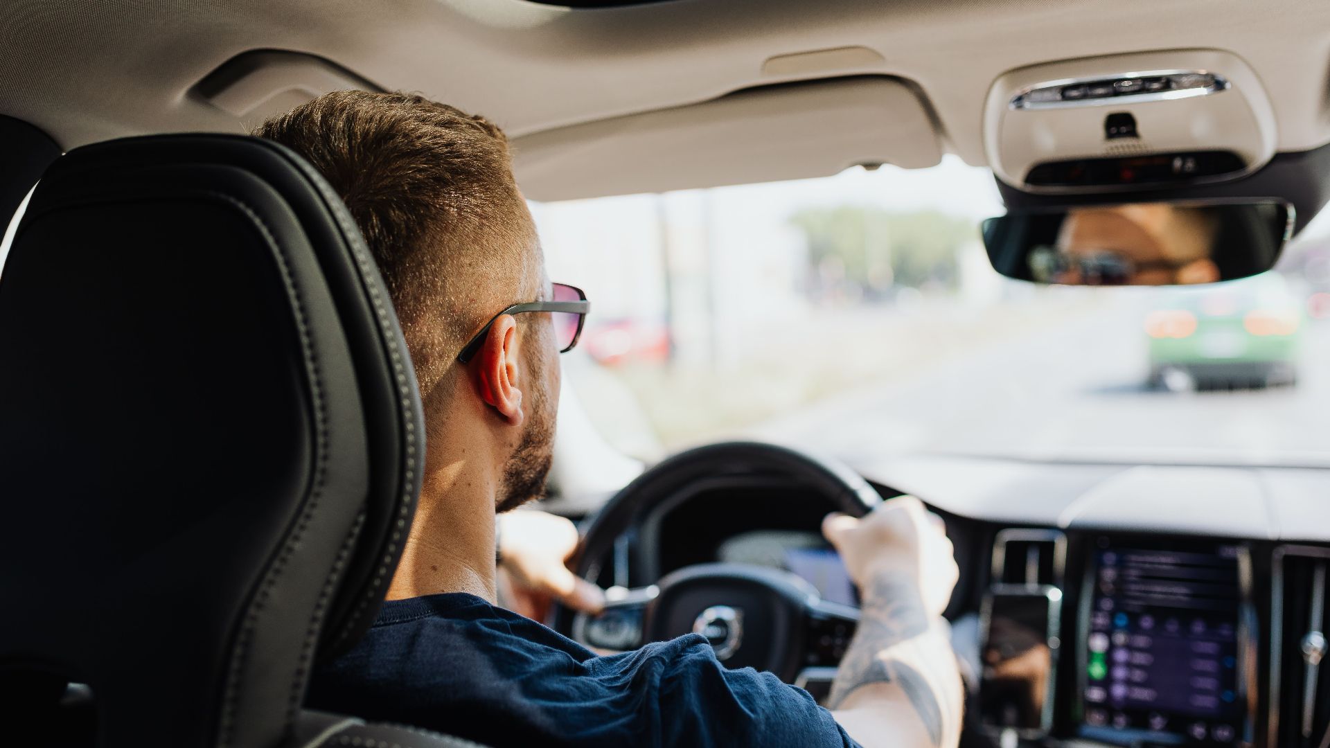 Rear view of a man driving a car with focus on interior details and steering.