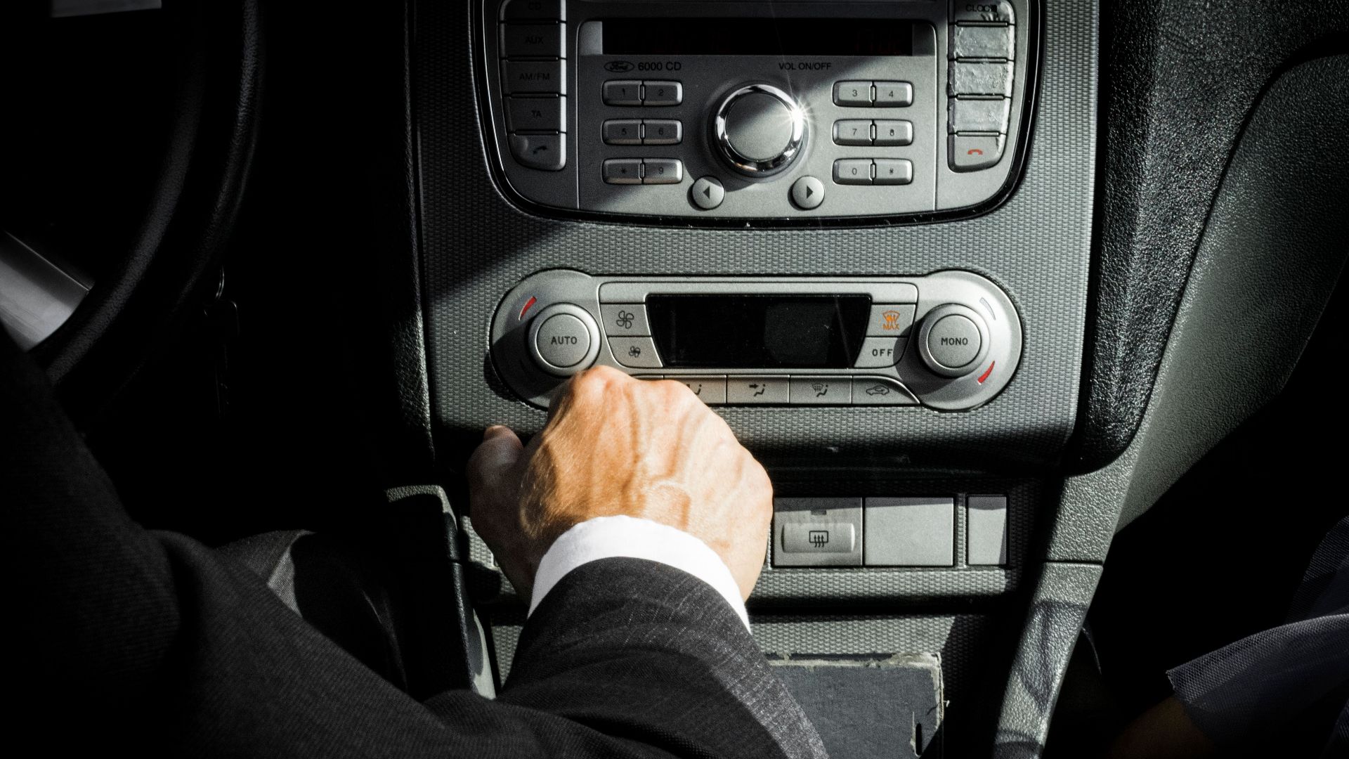 Close-up of a driver in a suit operating the car dashboard controls, capturing a professional interior setting.