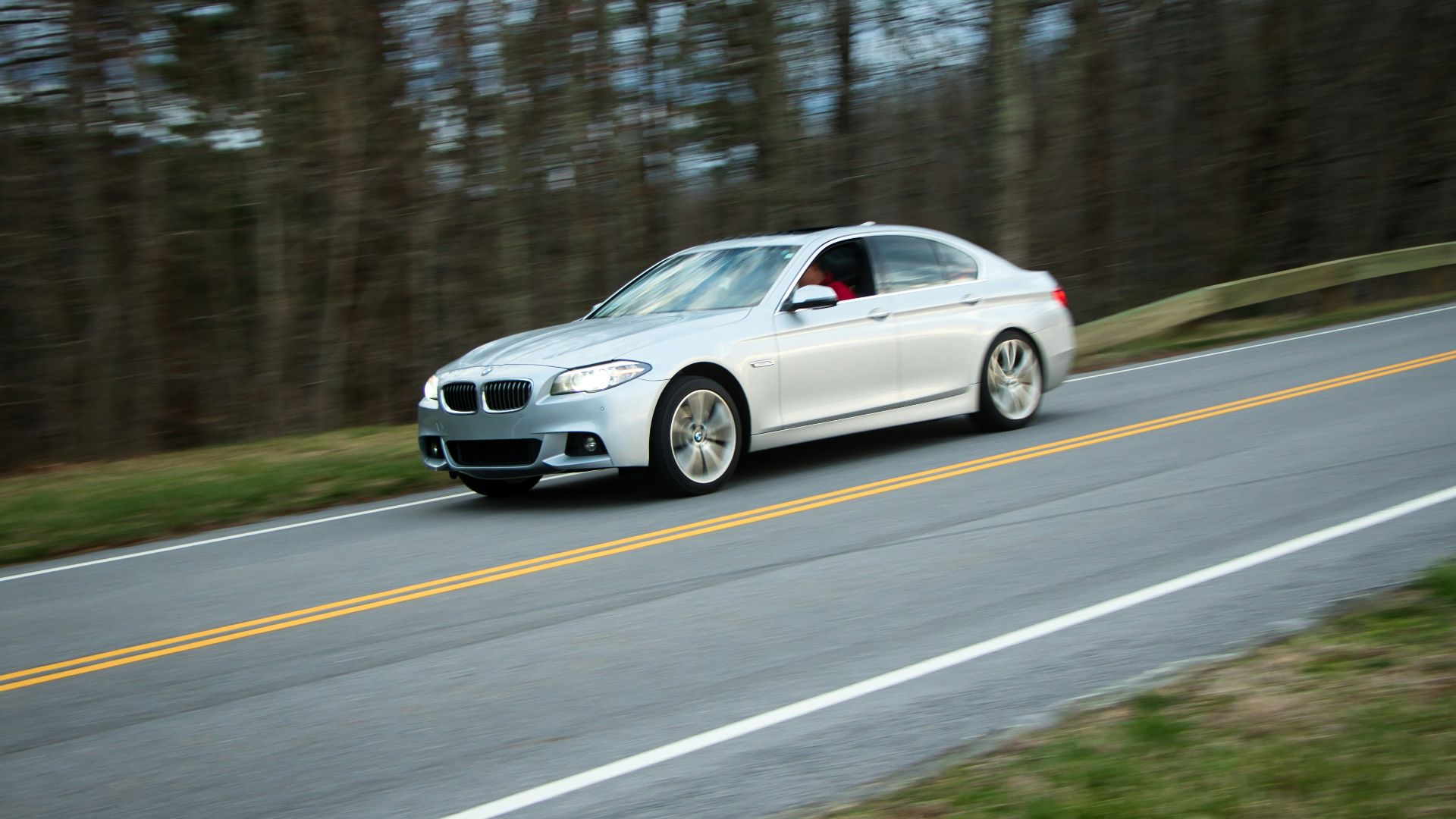 Silver sedan driving on a tree-lined road
