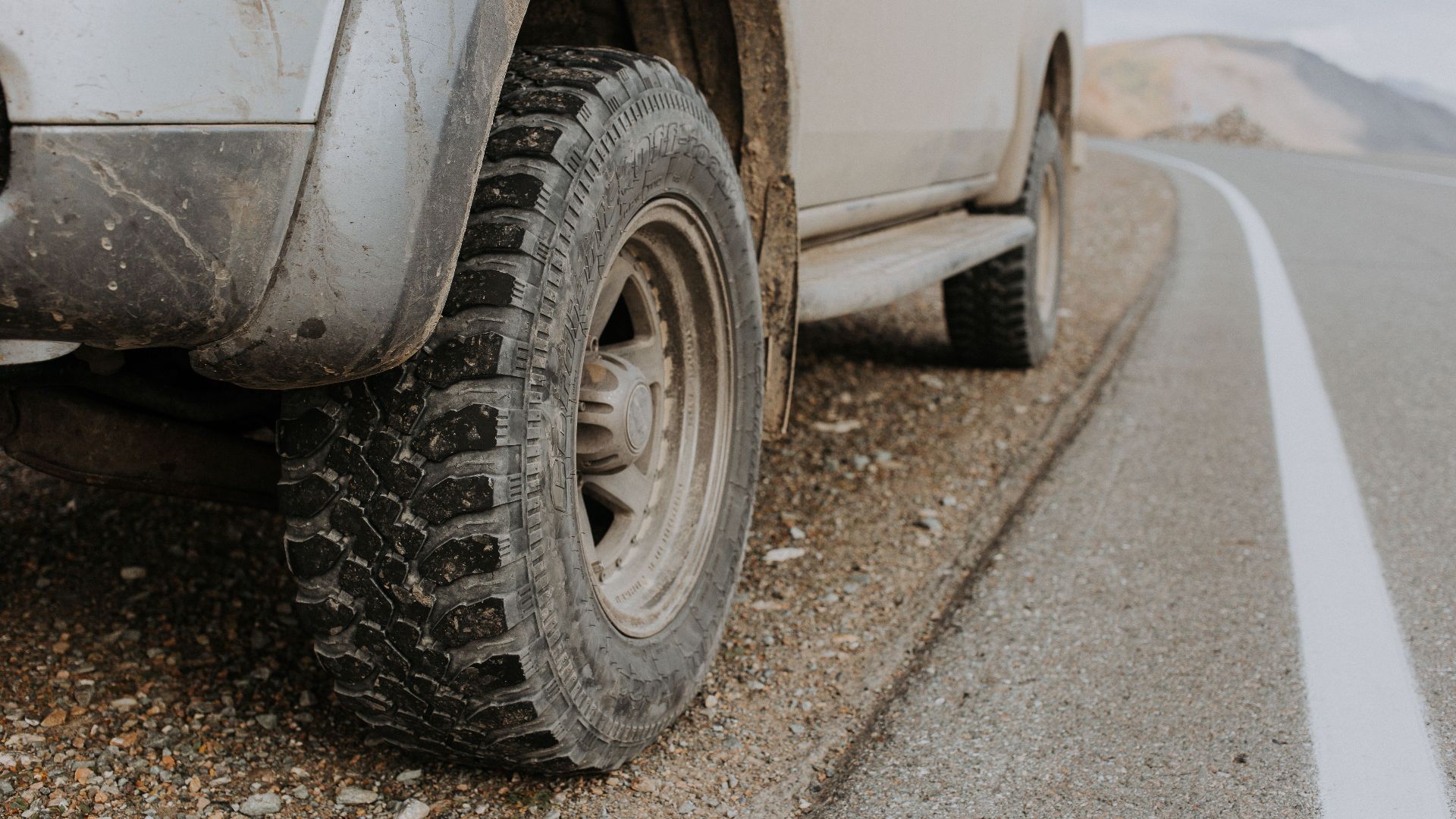 A rugged off-road vehicle's dirty tire on a gravel roadside in Altai Republic, Russia.