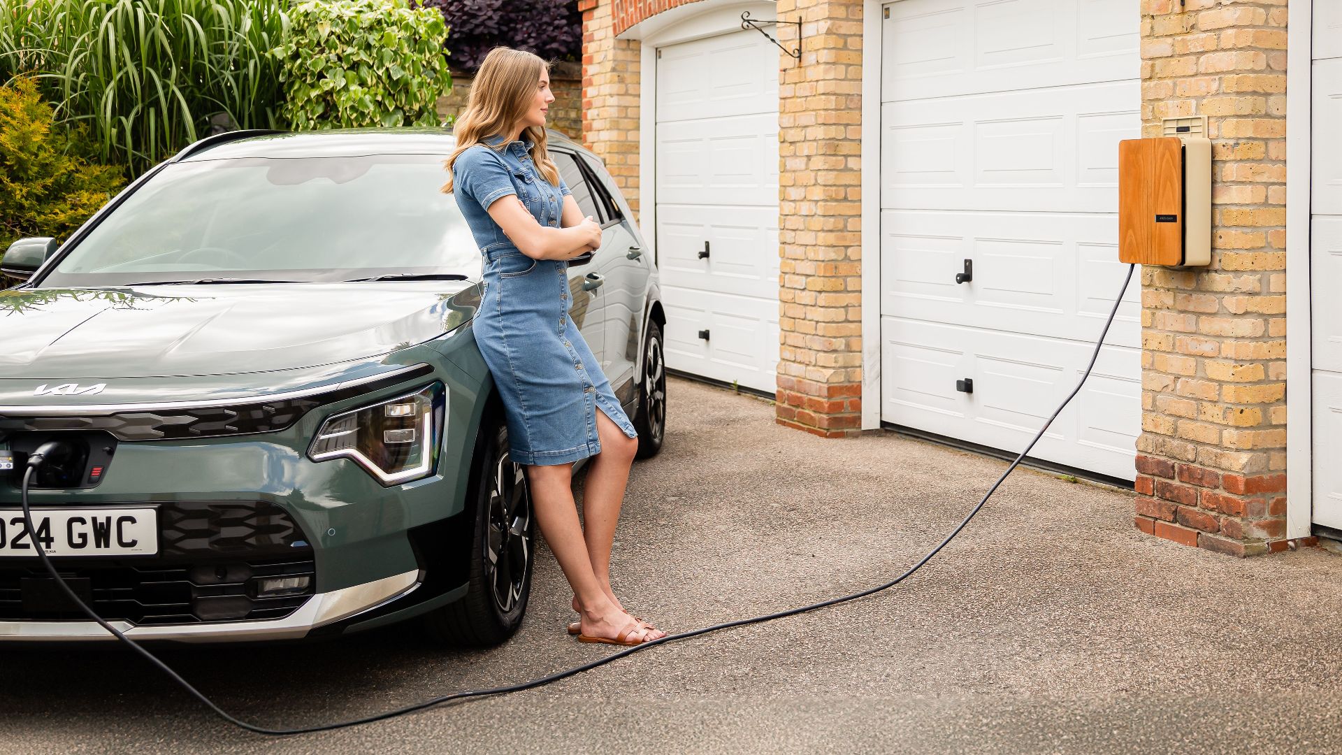 Woman charging electric vehicle at home with a modern wall-mounted charging station.