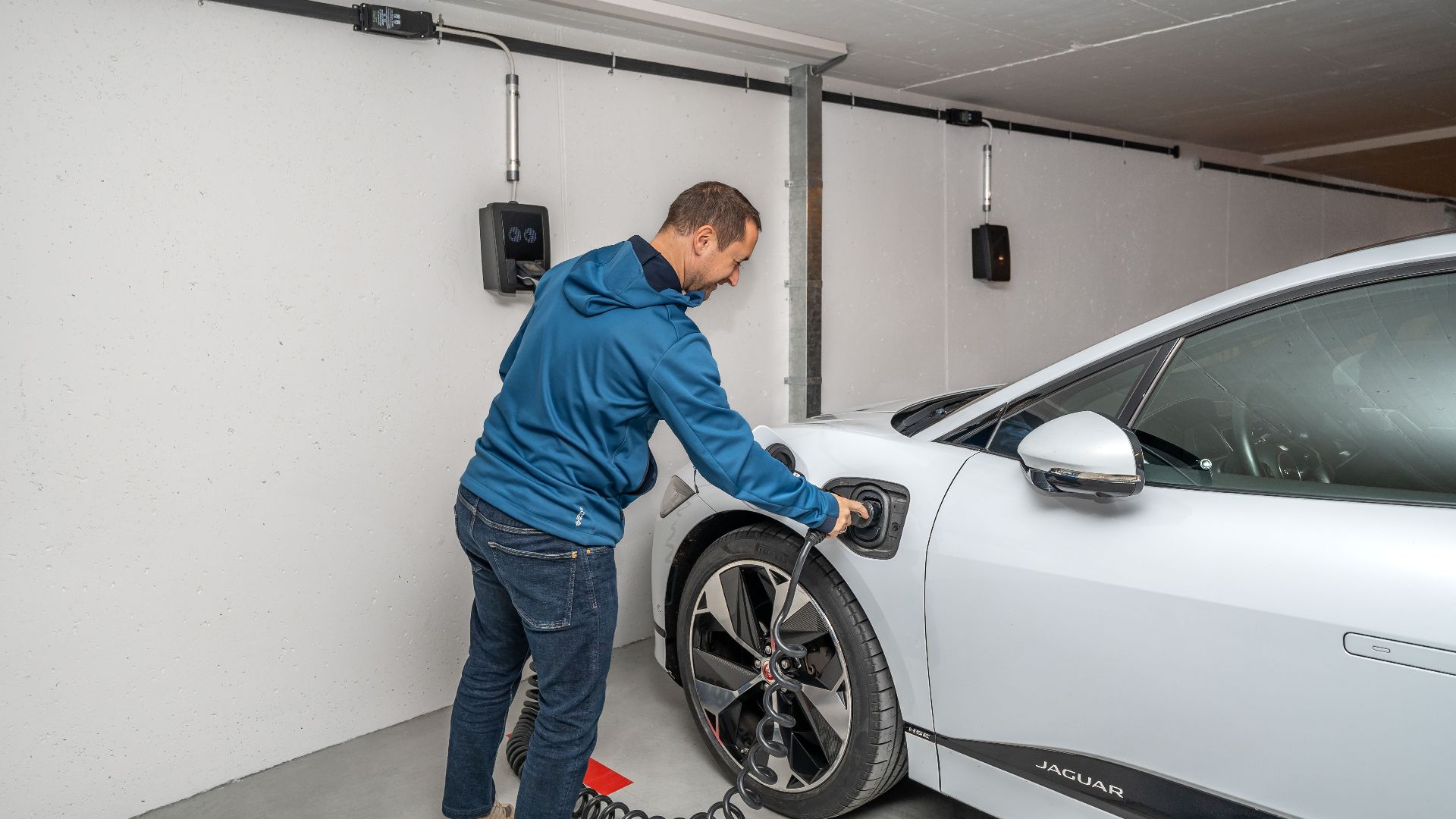 A man connects an electric car to a charging station in a modern indoor garage setting.