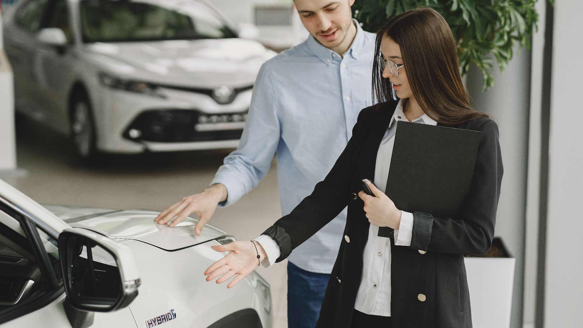 A man and saleswoman discussing a hybrid vehicle's features in an indoor showroom.