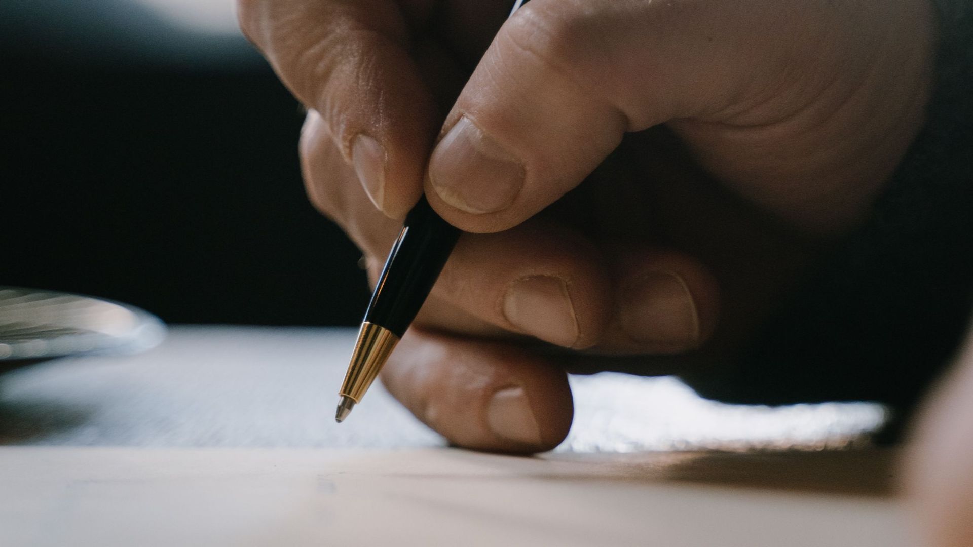 Detail shot of a hand holding a pen, writing on paper with blurred background.