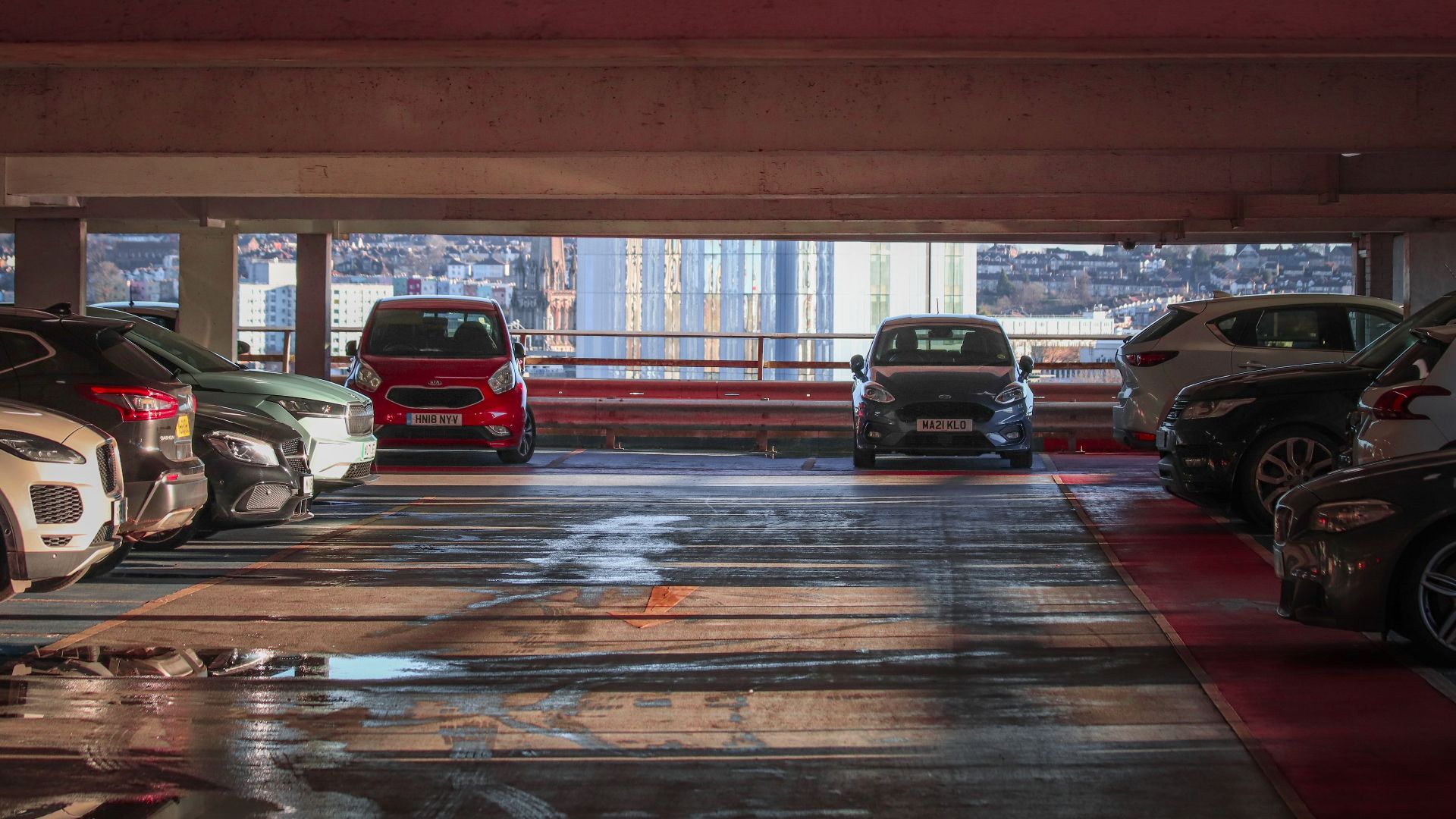 Parked cars in a multi-level parking garage overlooking a cityscape.